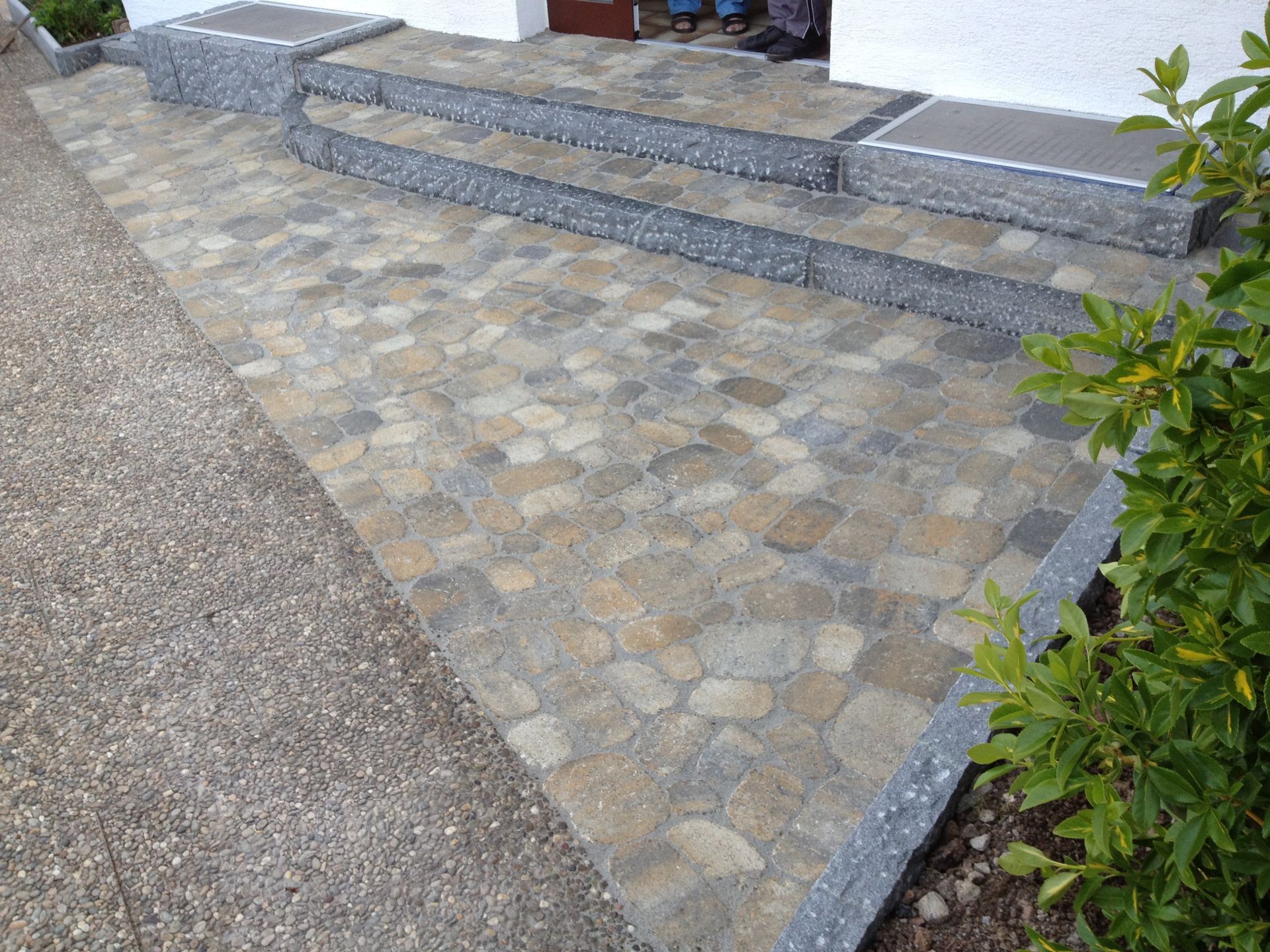 Steintreppe und Gehweg, die zu einem Eingang führen, aus Kopfsteinpflaster und grauen Steinbordüren.