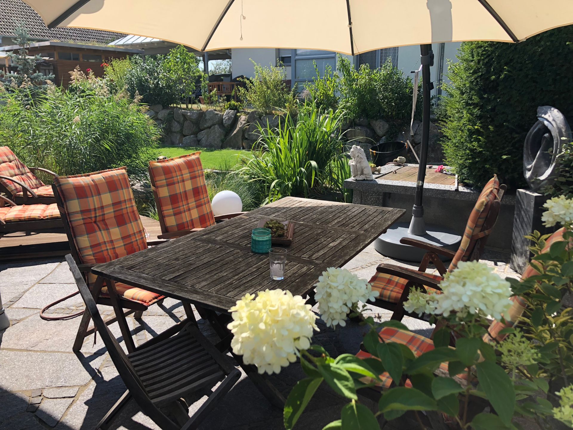 Essbereich im Freien unter einem Sonnenschirm in einem Garten mit Pflanzen und Steinmauern.