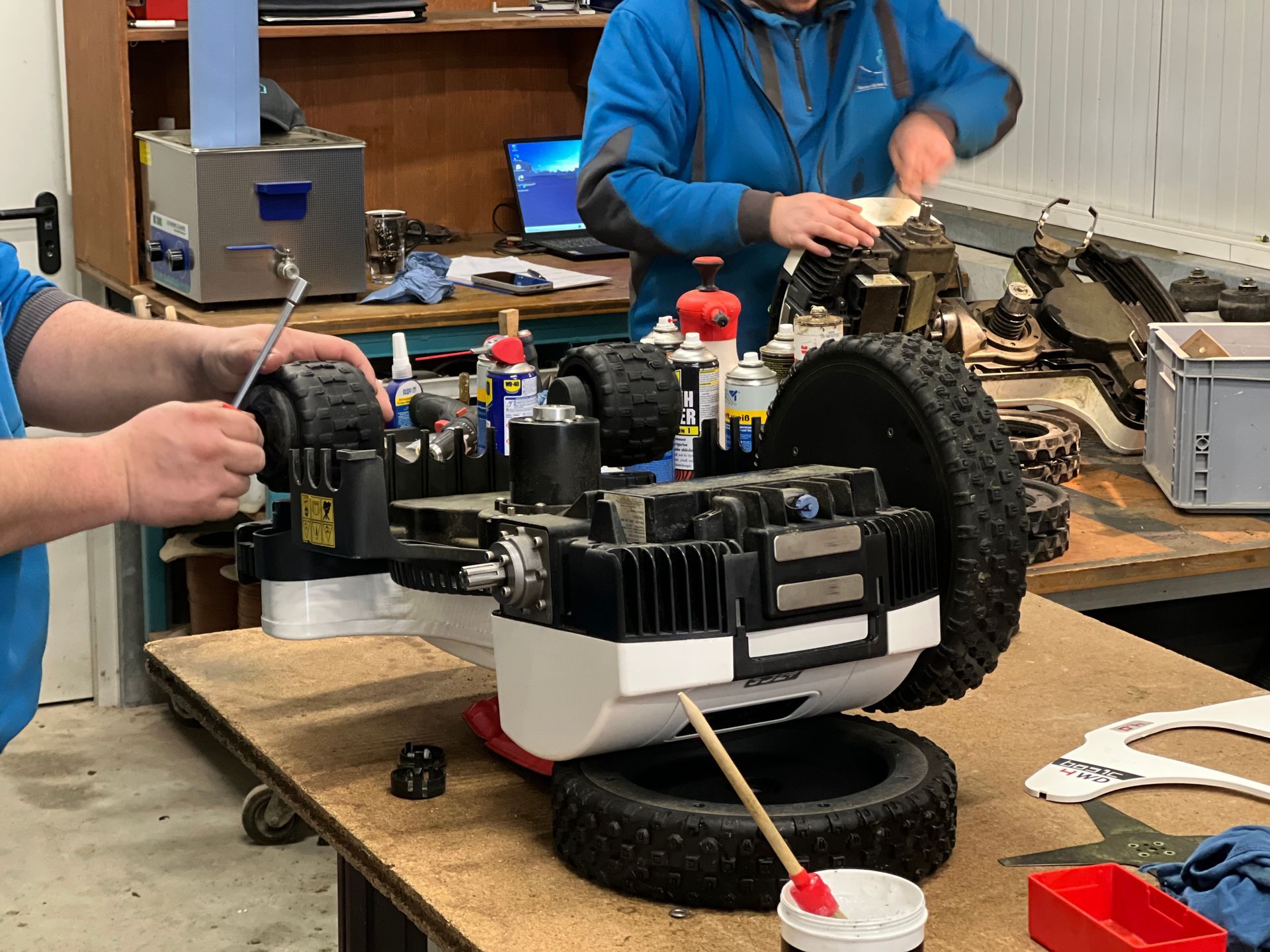 Zwei Personen arbeiten in einer Werkstatt an einer kleinen Maschine, möglicherweise für den Außeneinsatz.