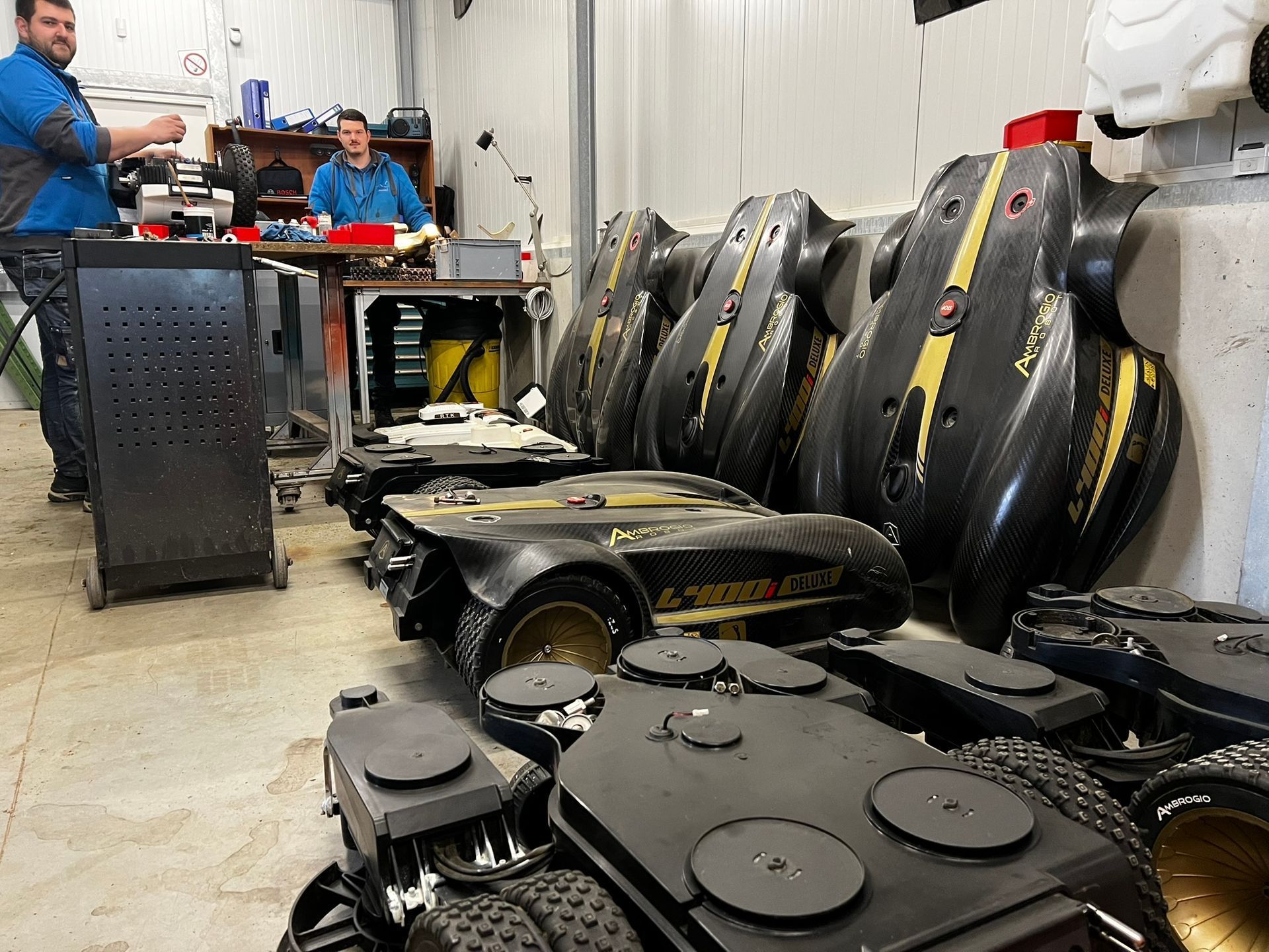 Zwei Personen in einer Werkstatt mit zerlegten schwarzen Robotern, einige mit goldenen Verzierungen, andere mit runden Oberteilen.