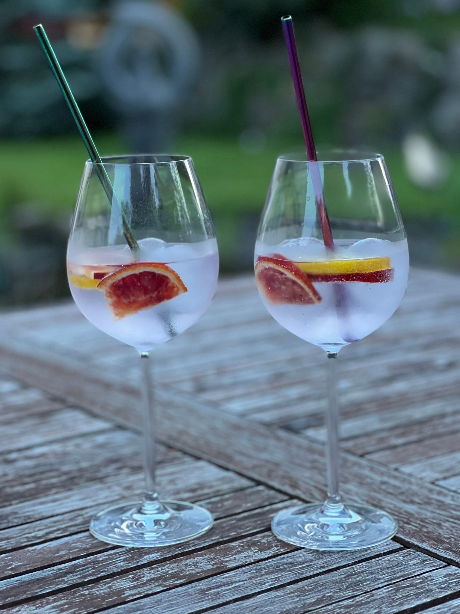 Zwei Gin Tonic mit Früchten und Strohhalmen auf einem Holztisch im Freien. Zwei Gin Tonic mit Früchten und Strohhalmen auf einem Holztisch im Freien.