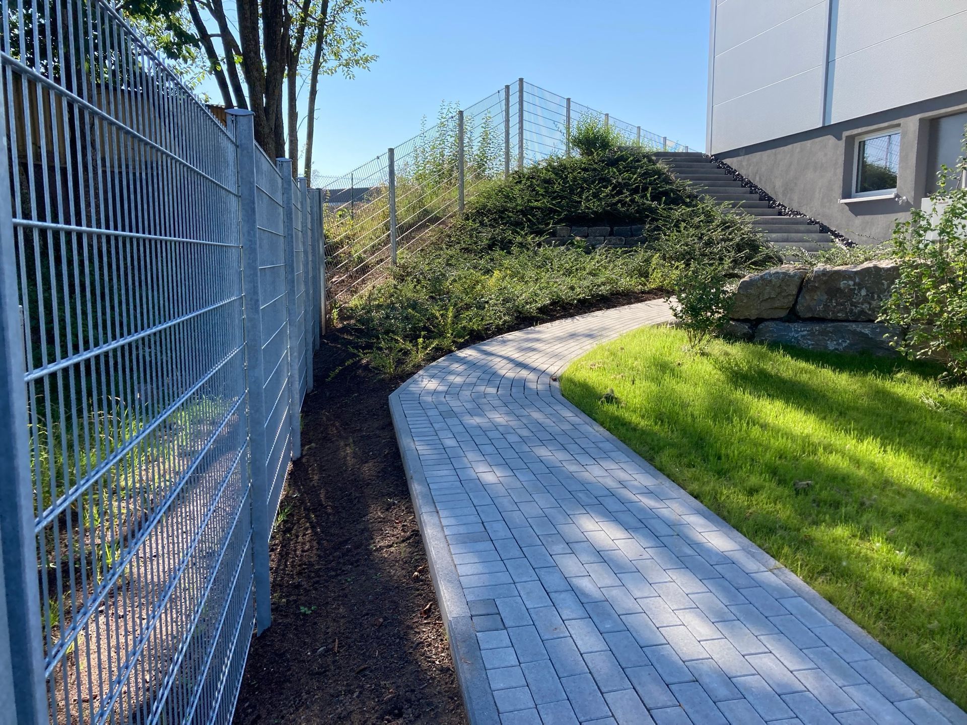 Ein Zaun umgibt einen gemauerten Weg, der zu einem Haus führt.