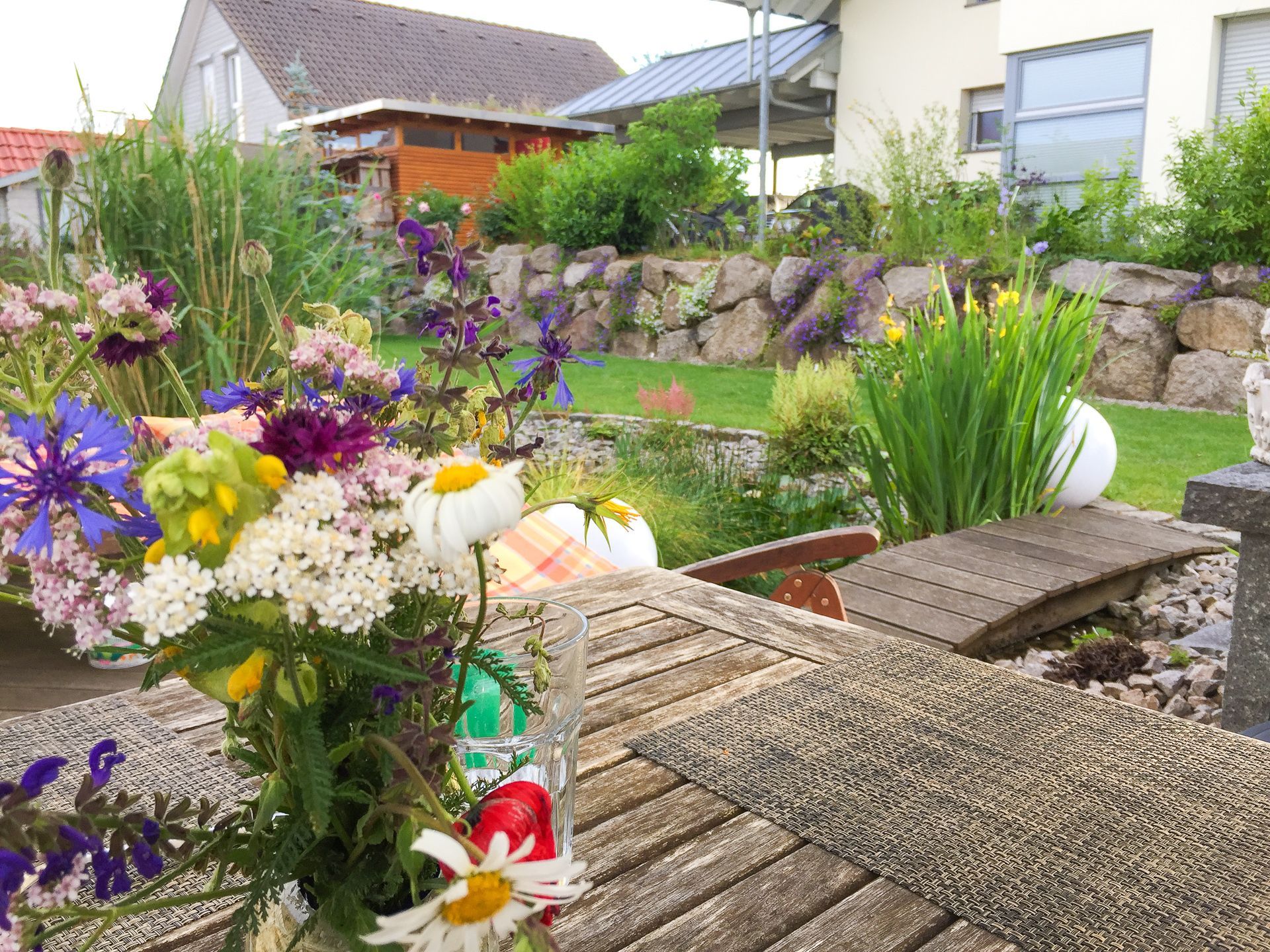 Eine Vase mit Blumen steht auf einem Holztisch in einem Garten