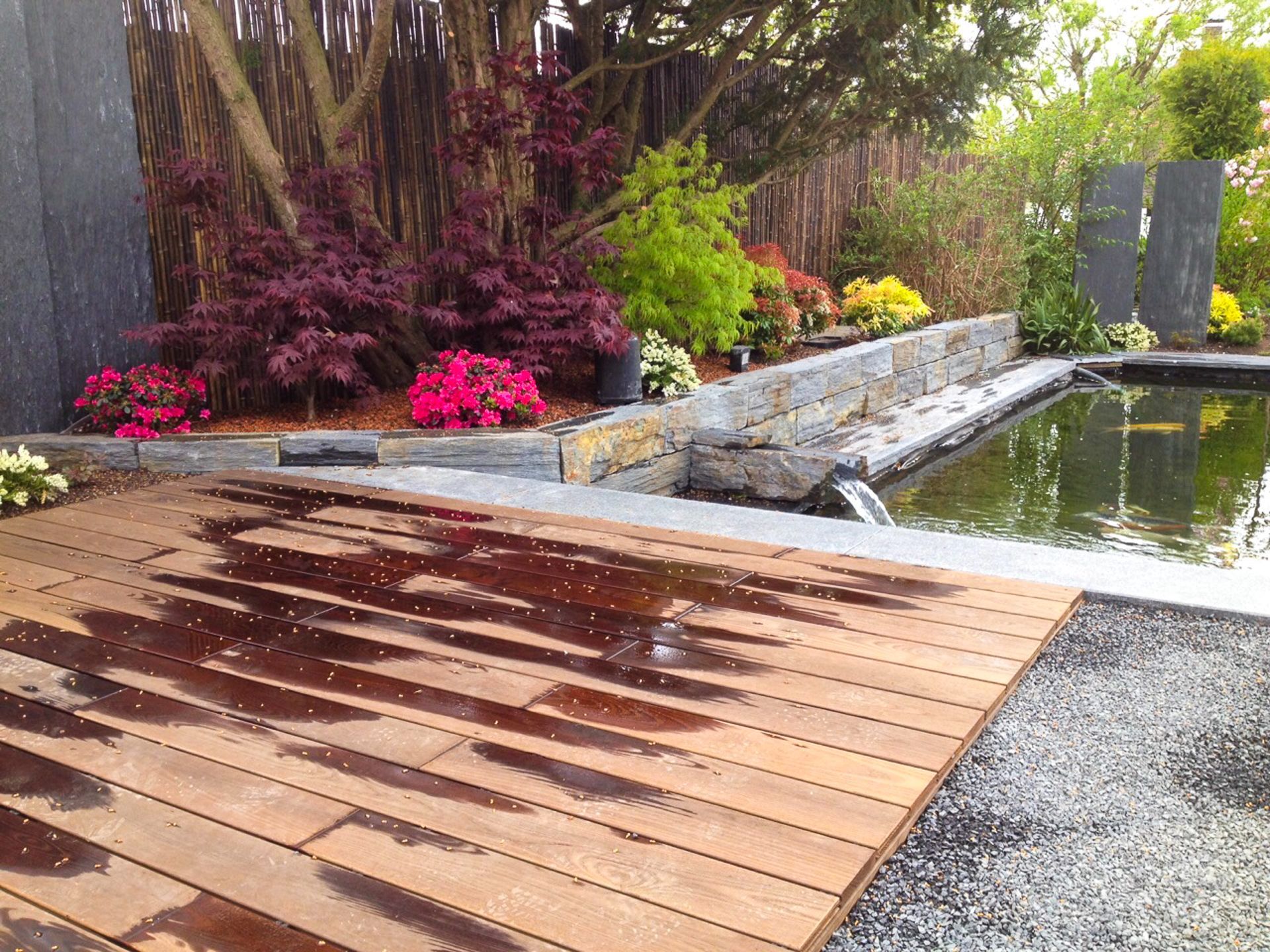 Neben einem Teich in einem Garten steht ein Holzdeck.
