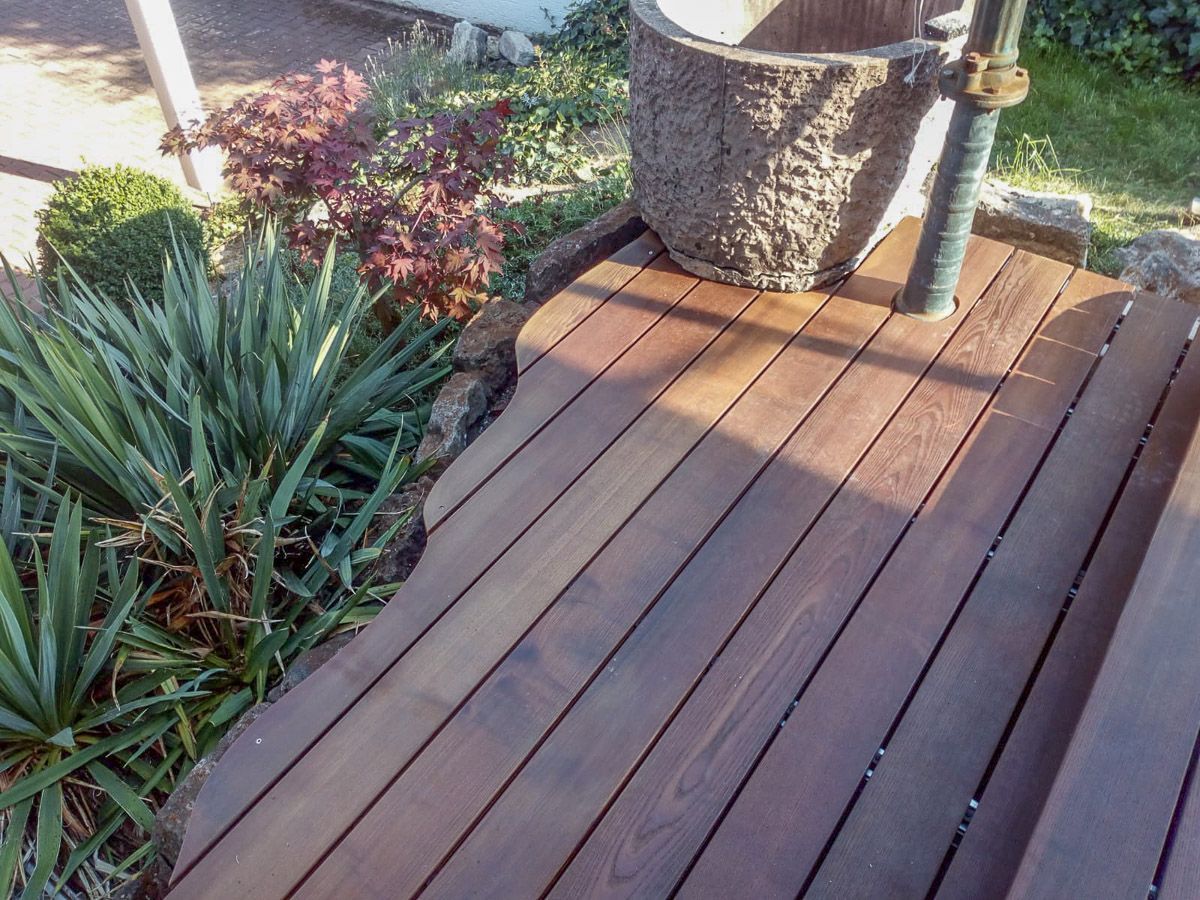 Ein Holzdeck mit einer Topfpflanze im Hintergrund.