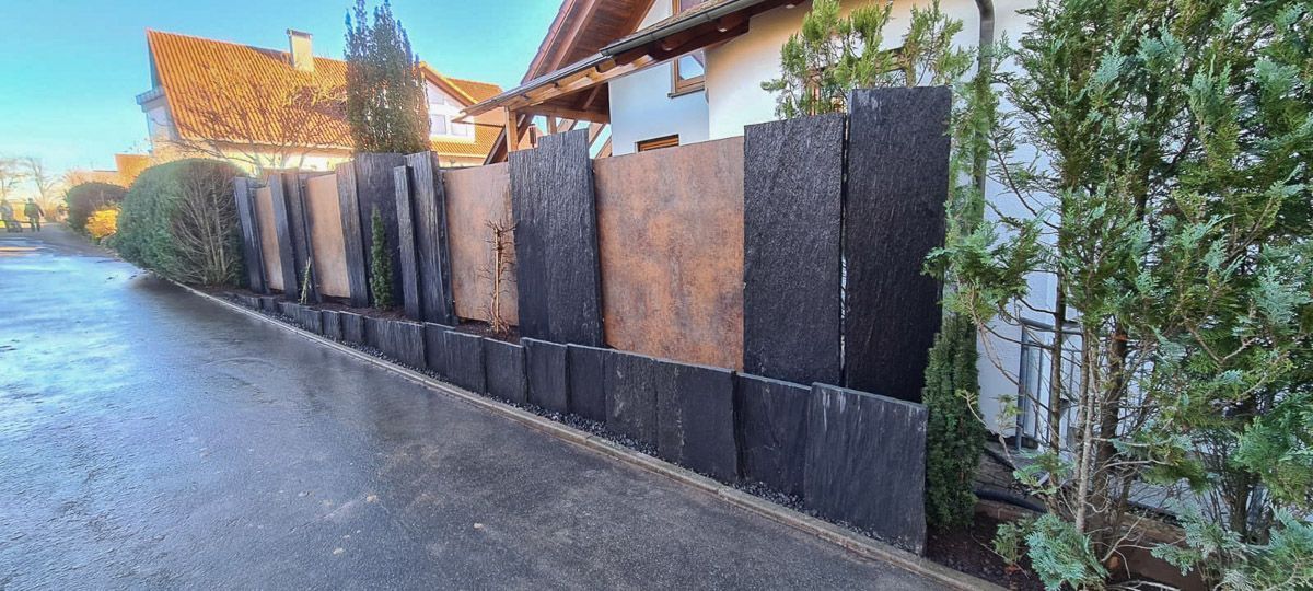 Neben einem Haus steht am Straßenrand ein Zaun.