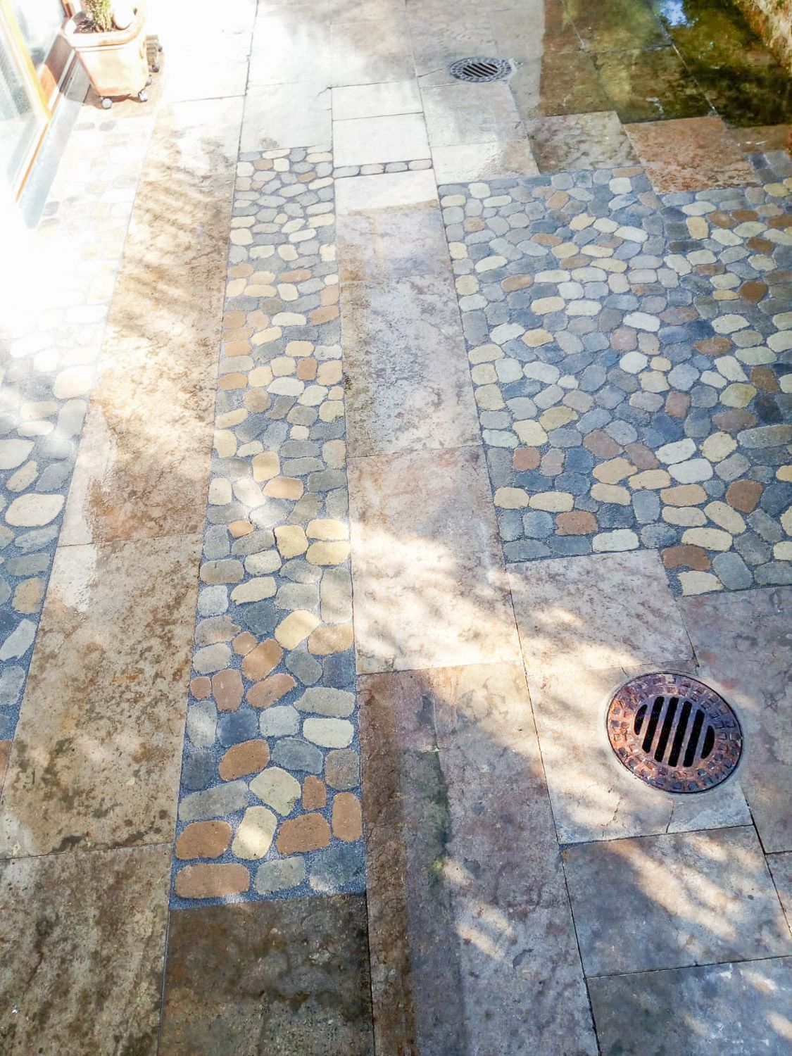 Neben einem Steinweg liegt ein Gullydeckel auf dem Boden.