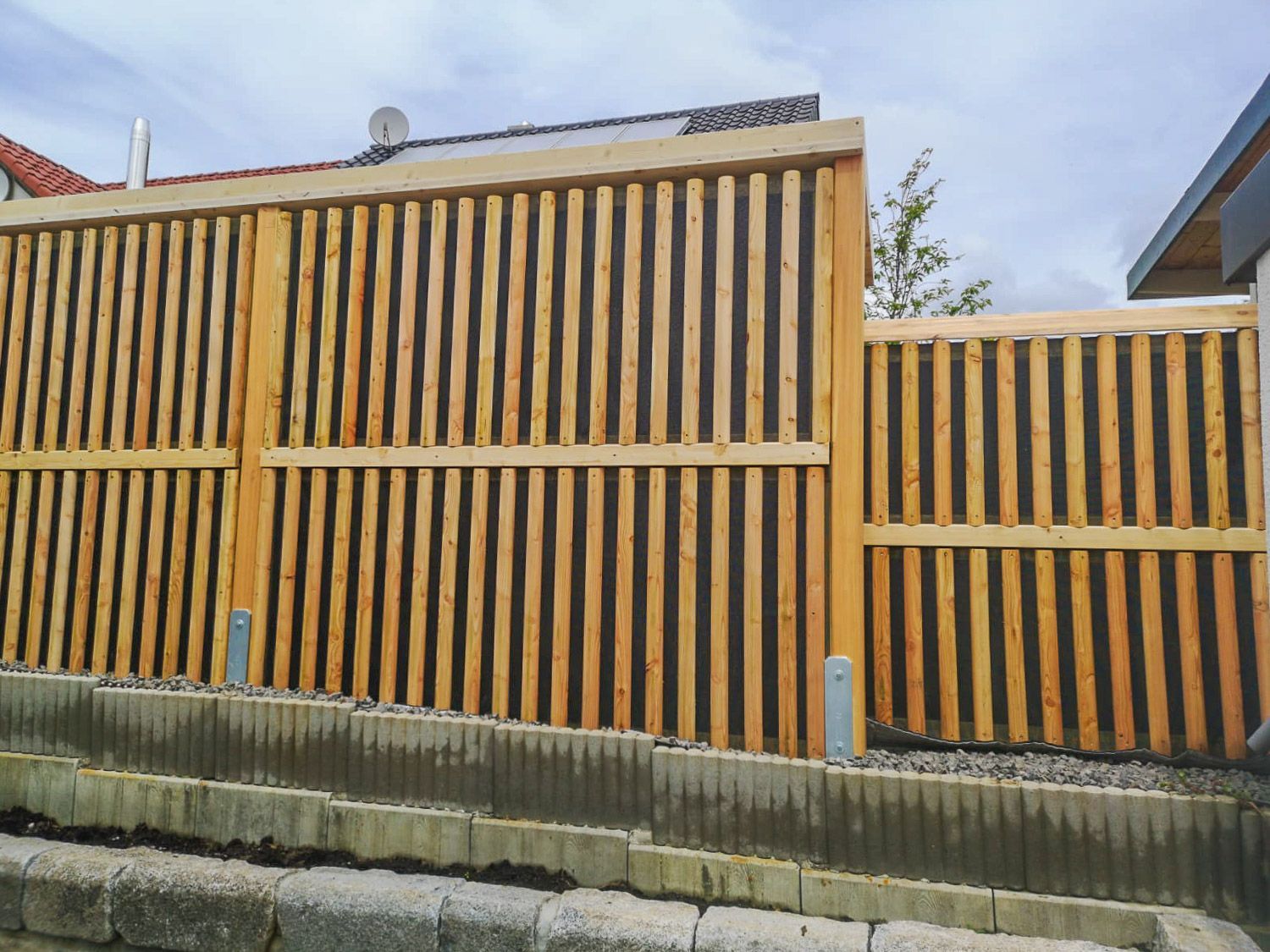 Neben einer Backsteinmauer steht ein Holzzaun.