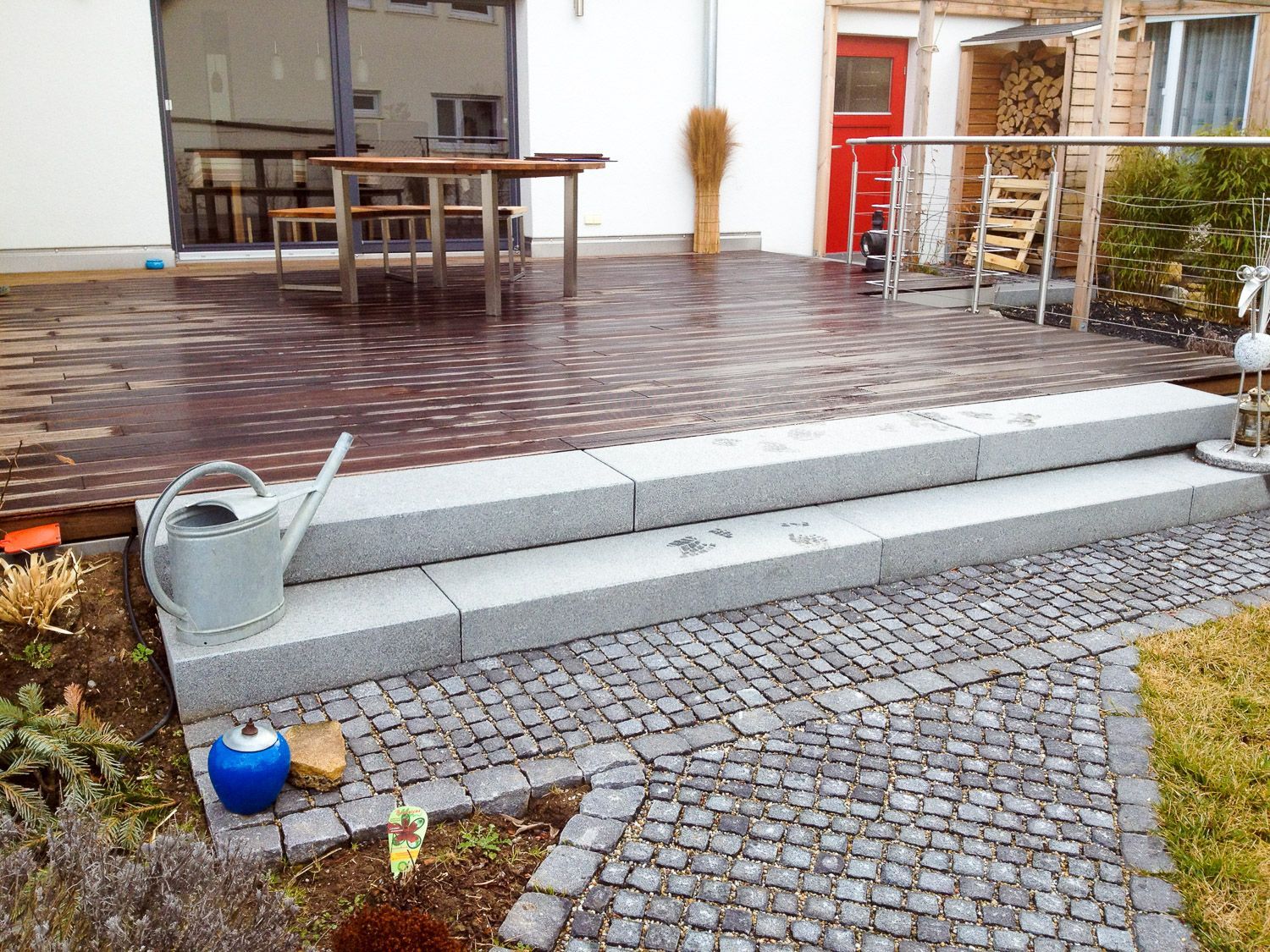 An der Seite einer Treppe, die zu einem Deck führt, steht eine Gießkanne.