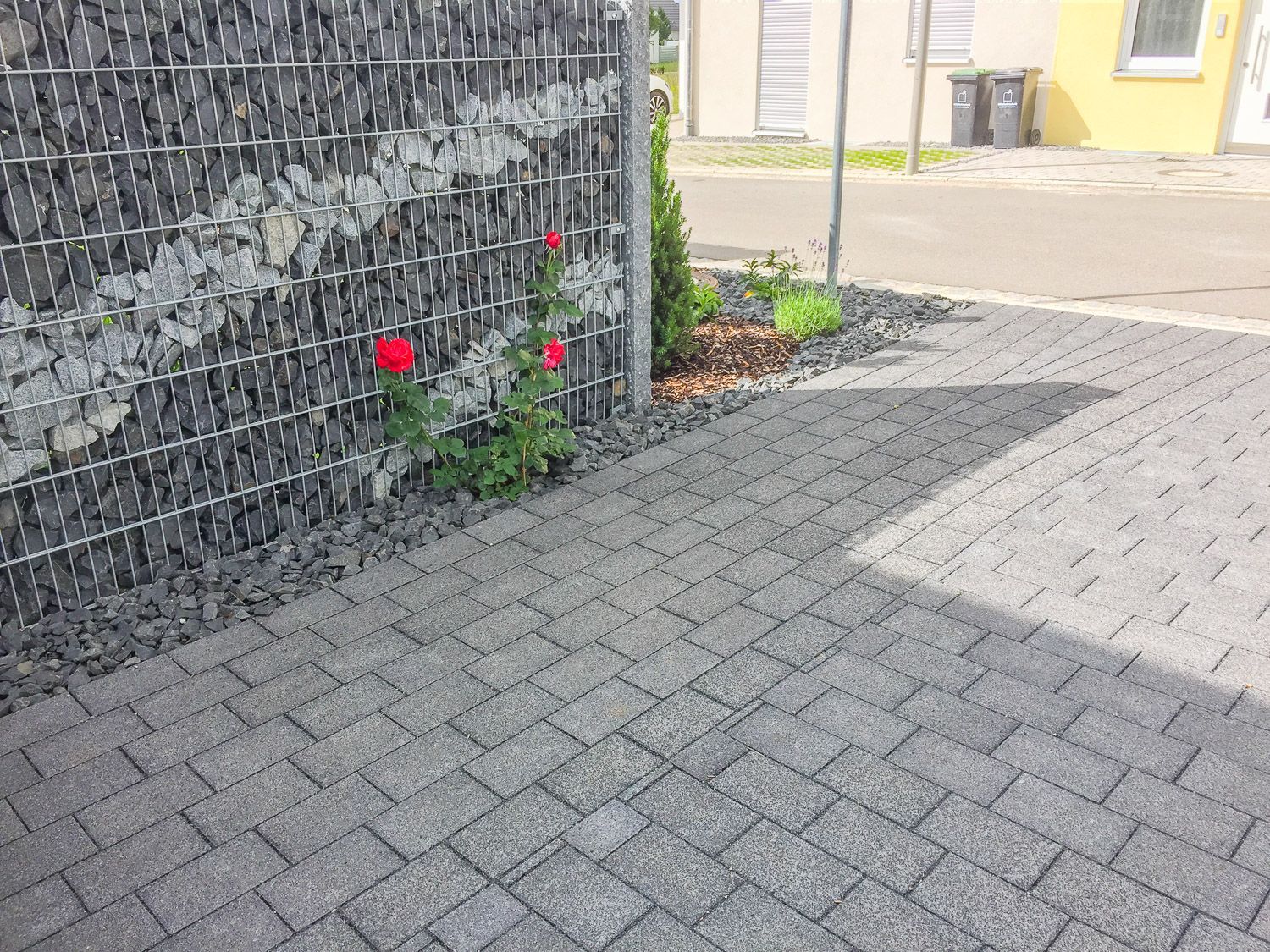 Eine gepflasterte Auffahrt mit einem Zaun und Blumen im Hintergrund.