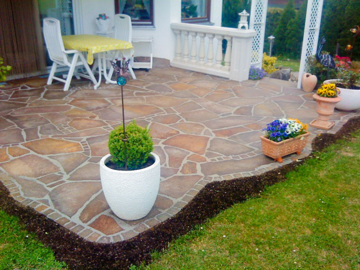 Eine Topfpflanze steht auf einer Terrasse neben einem Tisch und Stühlen.