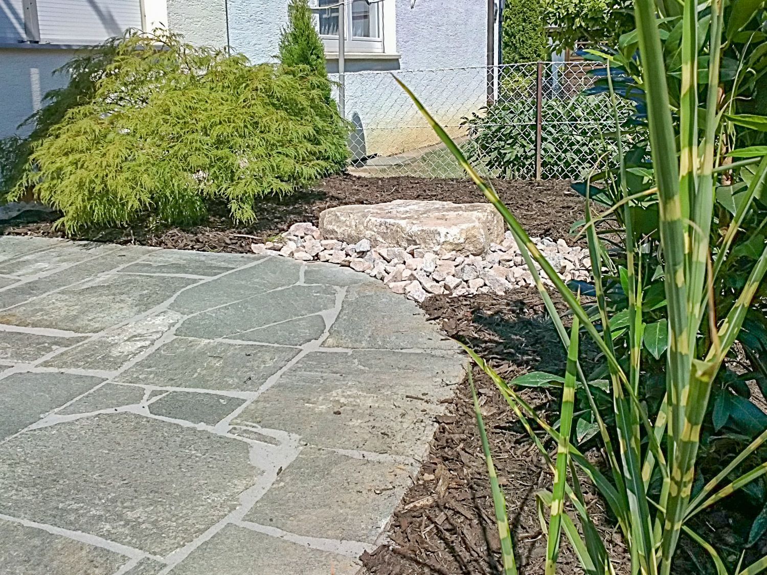 Ein Steinweg führt zu einem von Pflanzen und Felsen umgebenen Haus.