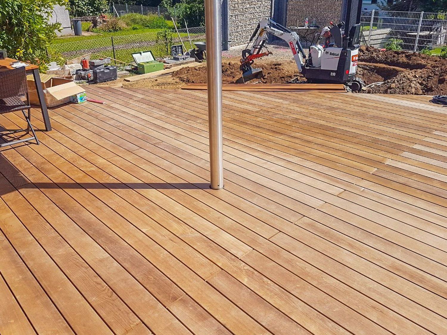 Ein Holzdeck mit einem kleinen Bagger im Hintergrund.