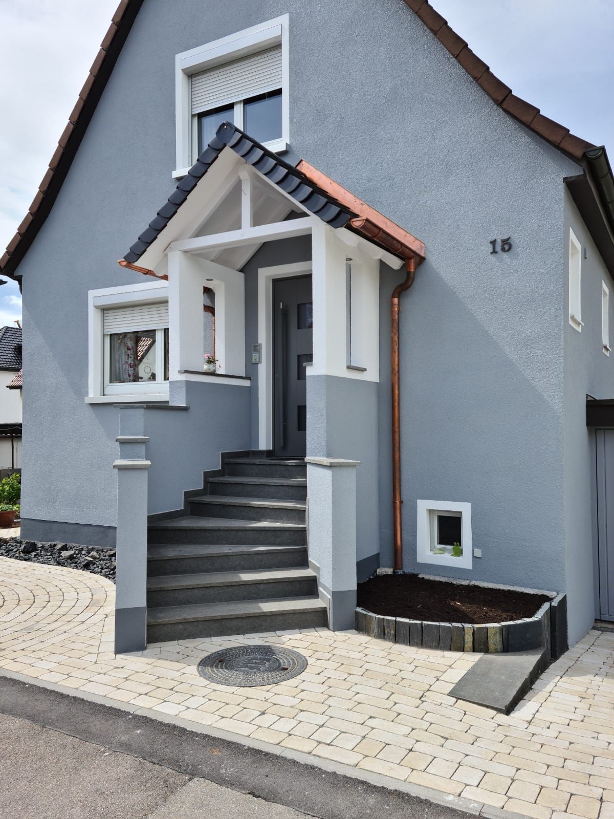 Graues Haus mit Eingangstreppe, Eingang unter einer überdachten Veranda und einem Steinweg.