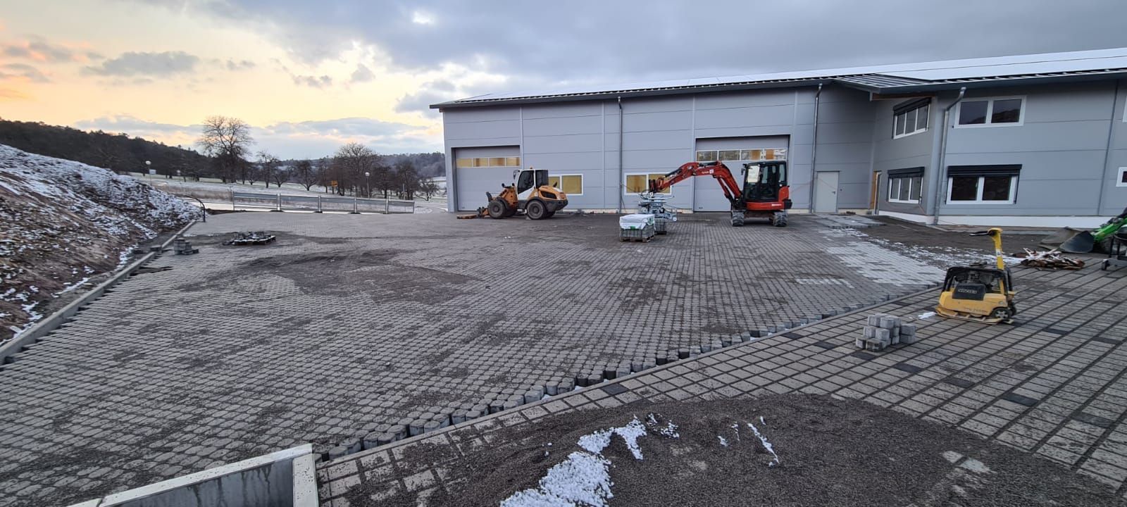 Baustelle mit verschiedenen Maschinen und einem Gebäude unter bewölktem Himmel.