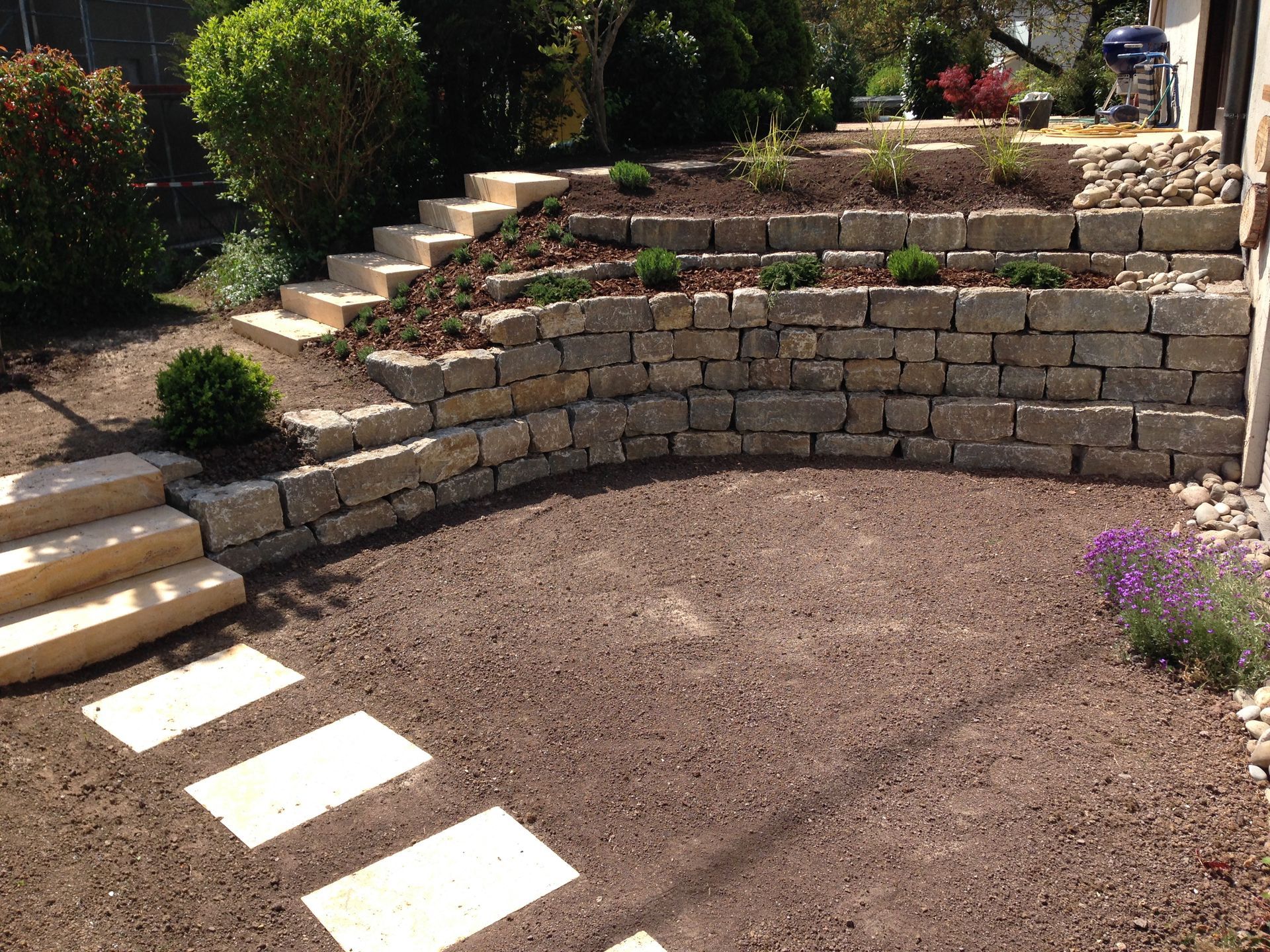 Steinstützmauer mit Stufen, mehreren Ebenen für Pflanzen und Steinweg.