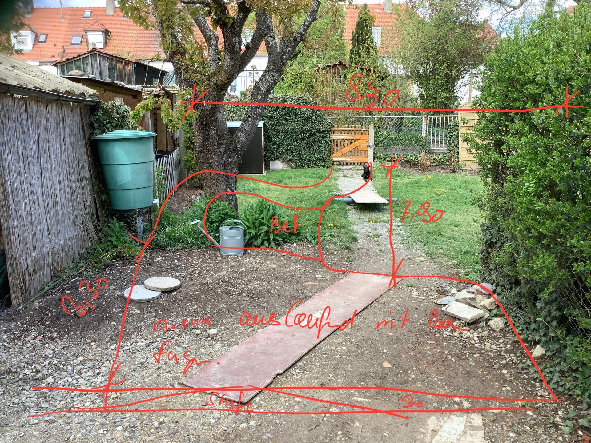 Hinterhof mit Kiesweg, braunem Holzbrett, Bäumen, einem Wasserfass und einer grünen Hecke.