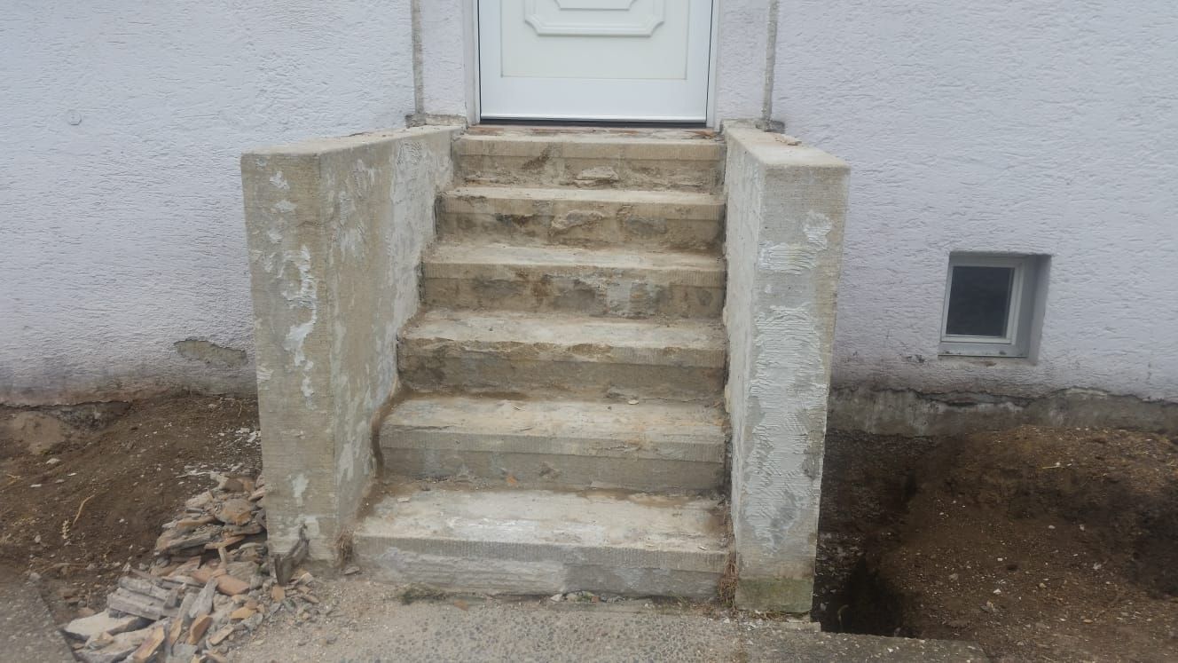 Betonstufen führen zu einer weißen Tür. Die Stufen sind abgenutzt und grau und bilden einen Kontrast zum weißen Gebäude.