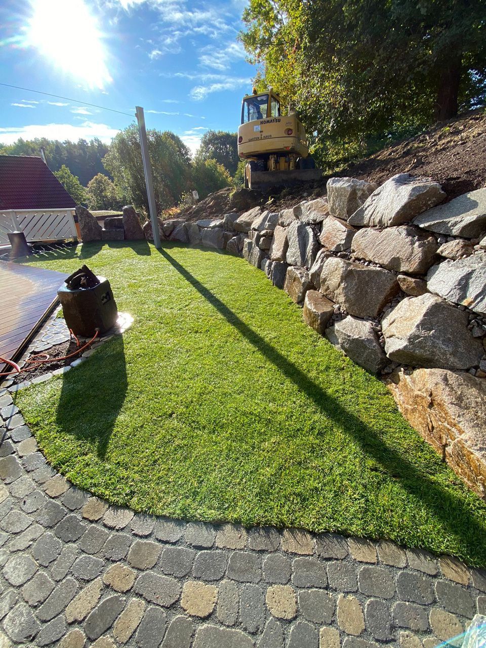 Auf einem üppigen grünen Rasen neben einer Steinmauer steht ein Bulldozer.