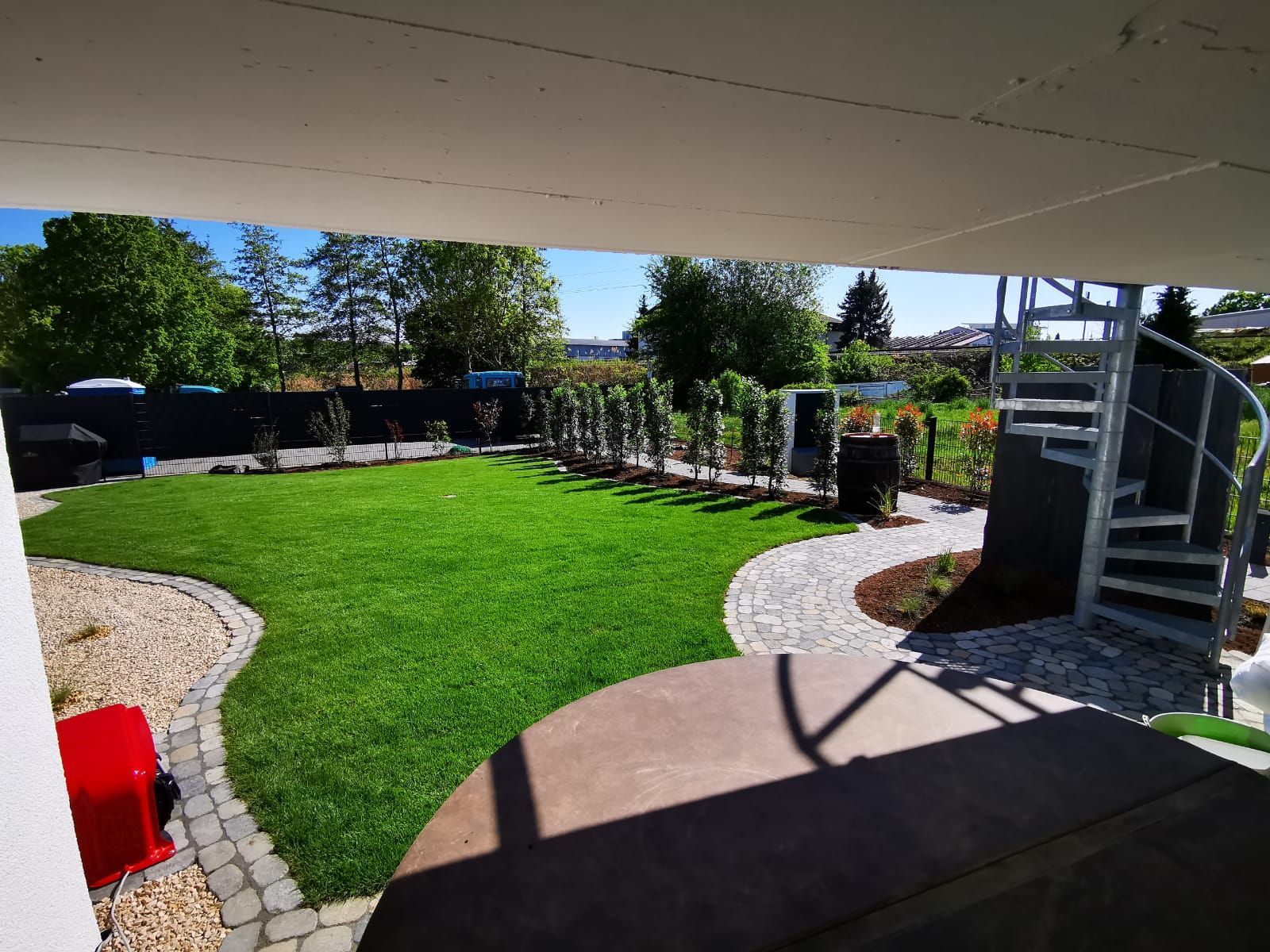 Üppig grüner Garten mit Wendeltreppe, Steinweg und gepflegtem Rasen. Blauer Himmel, sonniger Tag.