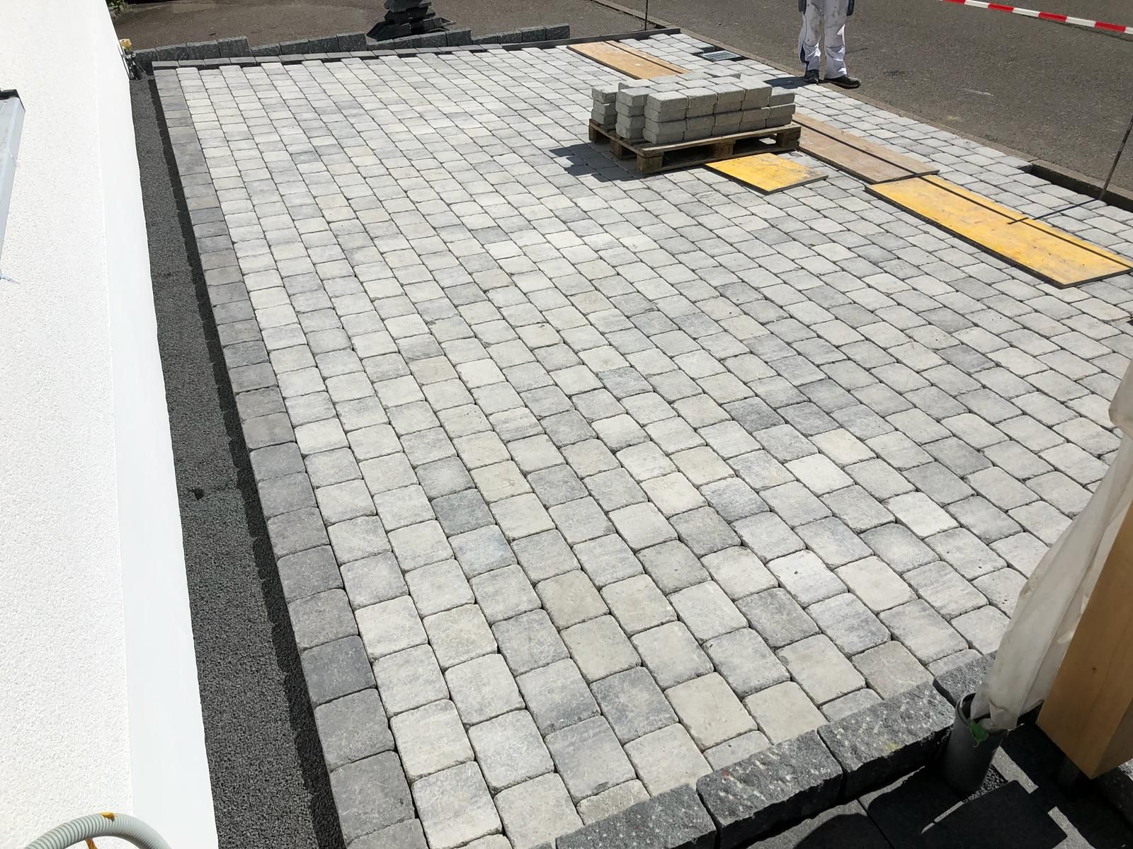 In der Nähe eines Gebäudes werden graue Pflastersteine ​​für eine Terrasse mit dunkelgrauer Umrandung verlegt.