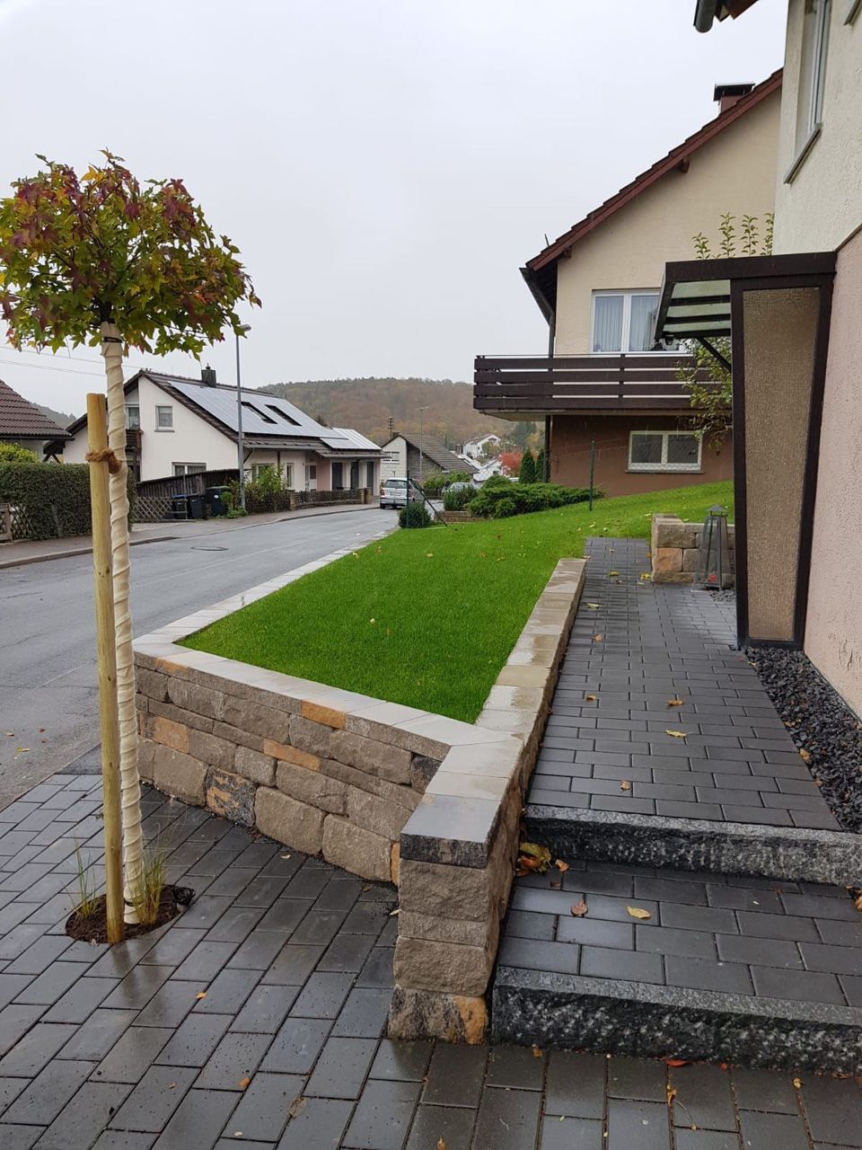 Ein gemauerter Gehweg, der zu einem Haus mit einem Baum davor führt