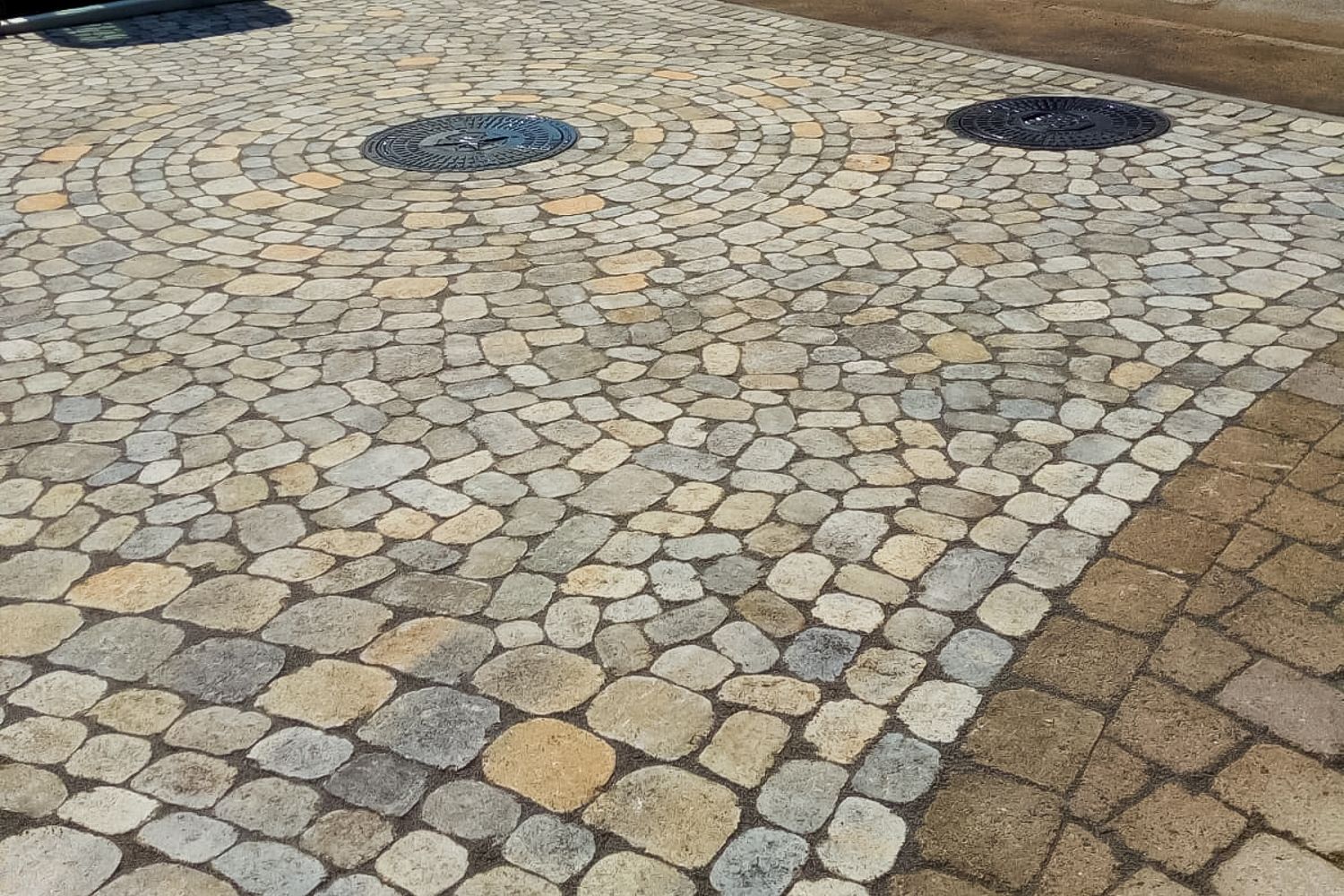 Eine gepflasterte Auffahrt mit einem Gullydeckel in der Mitte.