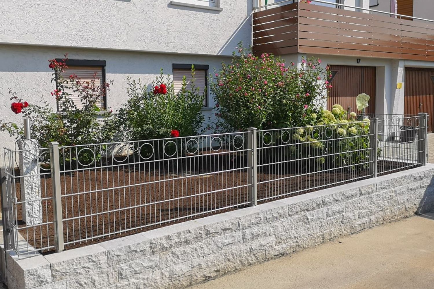 Ein Edelstahlzaun umgibt einen Garten vor einem Haus.