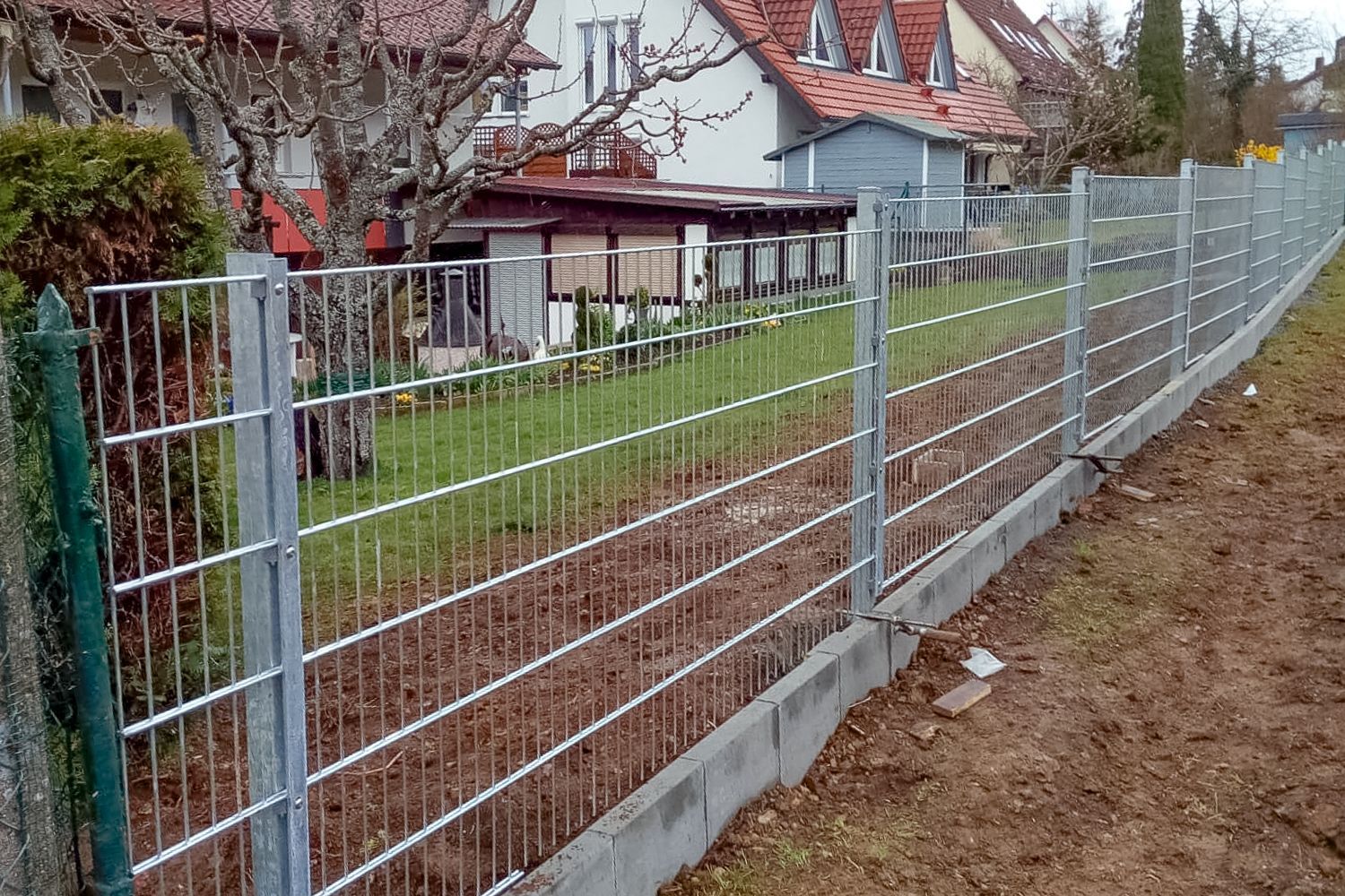 Ein Metallzaun umgibt einen Hof mit einem Haus im Hintergrund.