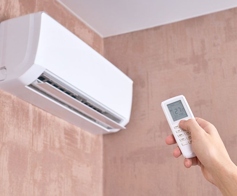 Eine Person hält eine Fernbedienung vor einer Klimaanlage.
