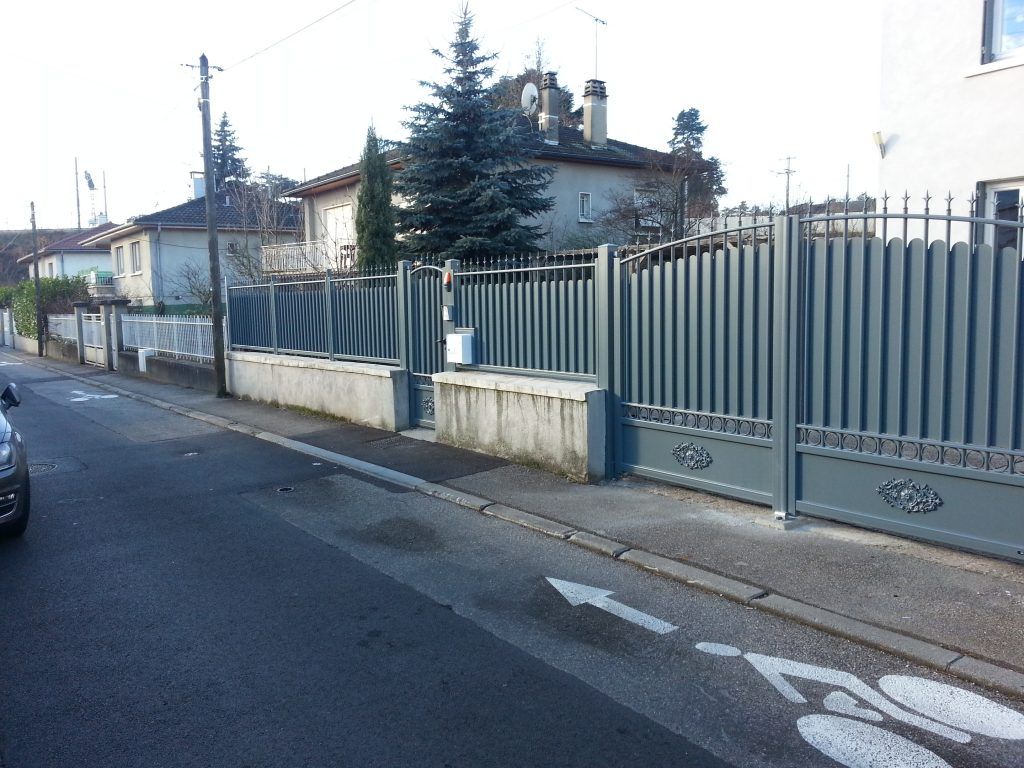 Une rue avec un portail battant et une clôture