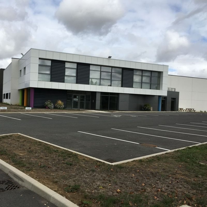 Un bâtiment commercial de deux étages avec un revêtement blanc, de grandes baies vitrées et un niveau inférieur gris foncé.