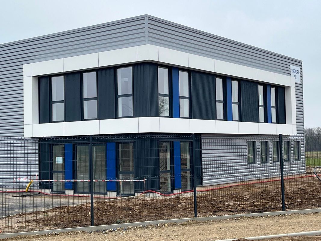 Un bâtiment commercial moderne de deux étages, caractérisé par une structure blanche, de grandes fenêtres et un revêtement métallique foncé.