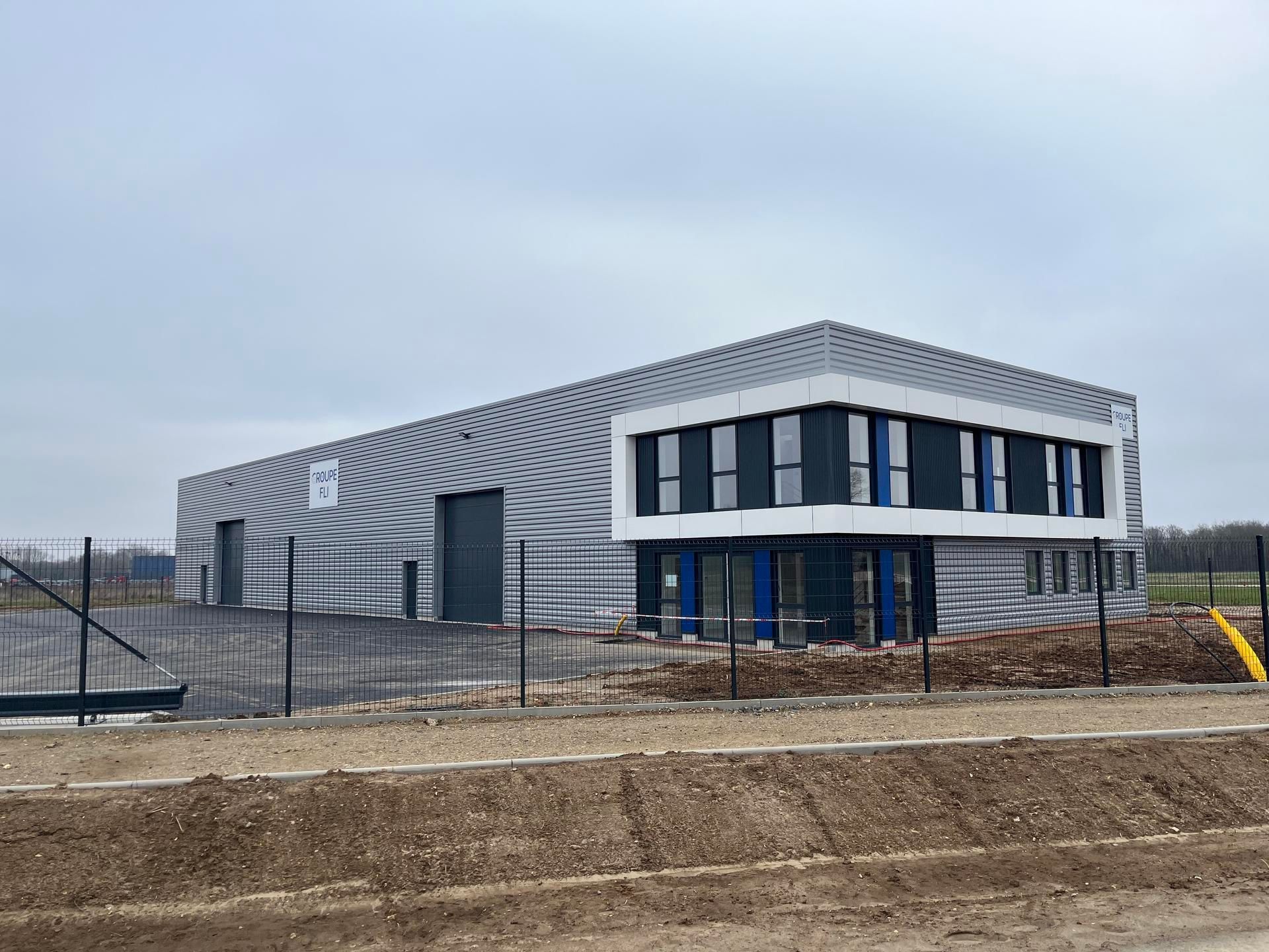 Un bâtiment industriel moderne avec un bardage en tôle ondulée grise et une partie à deux étages avec des panneaux sombres et des finitions blanches.