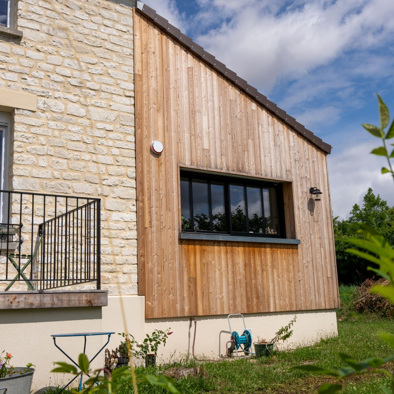 Une extension de maison revêtue de pierre et de bois, avec une fenêtre à cadre noir.