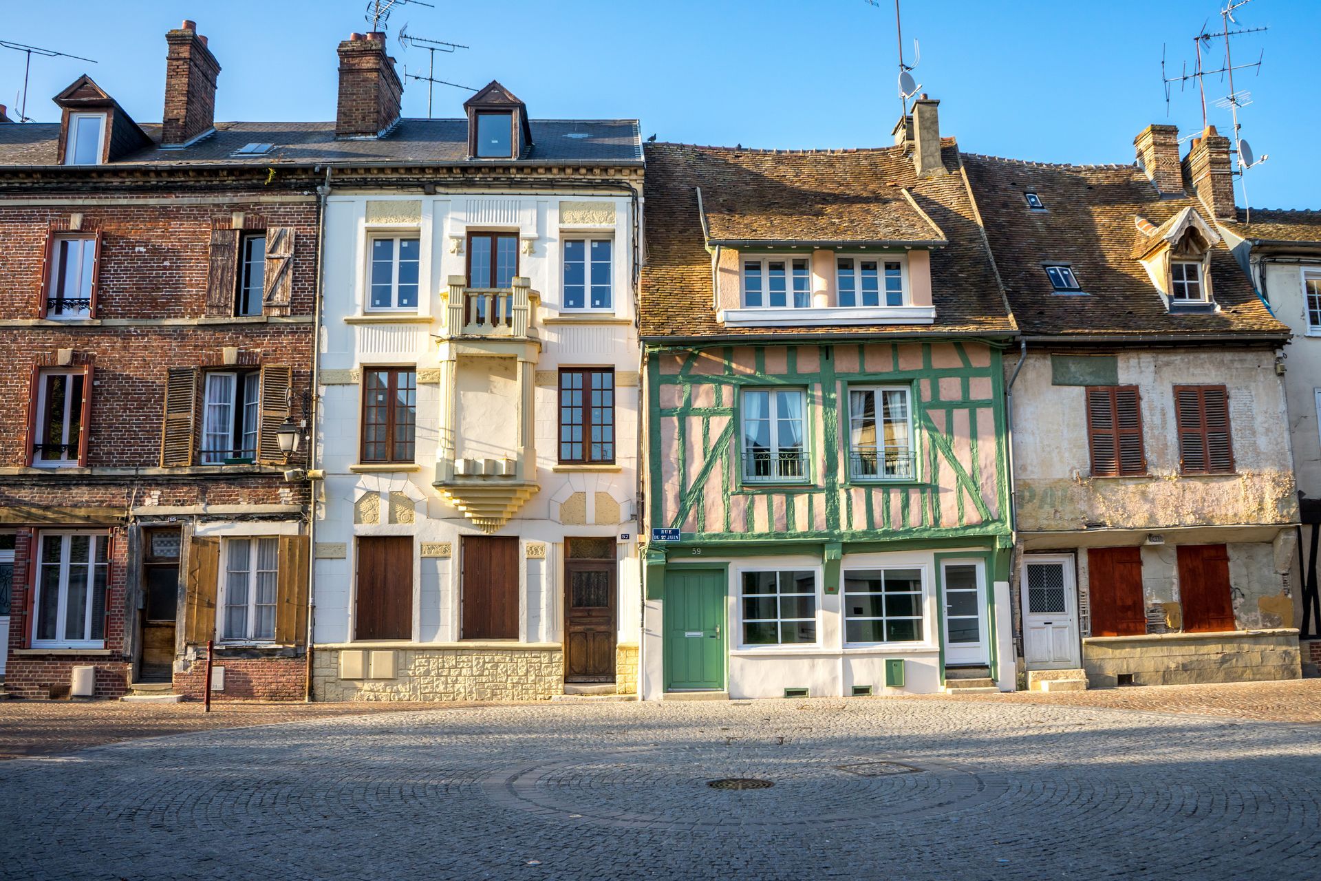 Quatre immeubles résidentiels historiques aux façades variées bordent une rue pavée sous un ciel d'un bleu limpide.