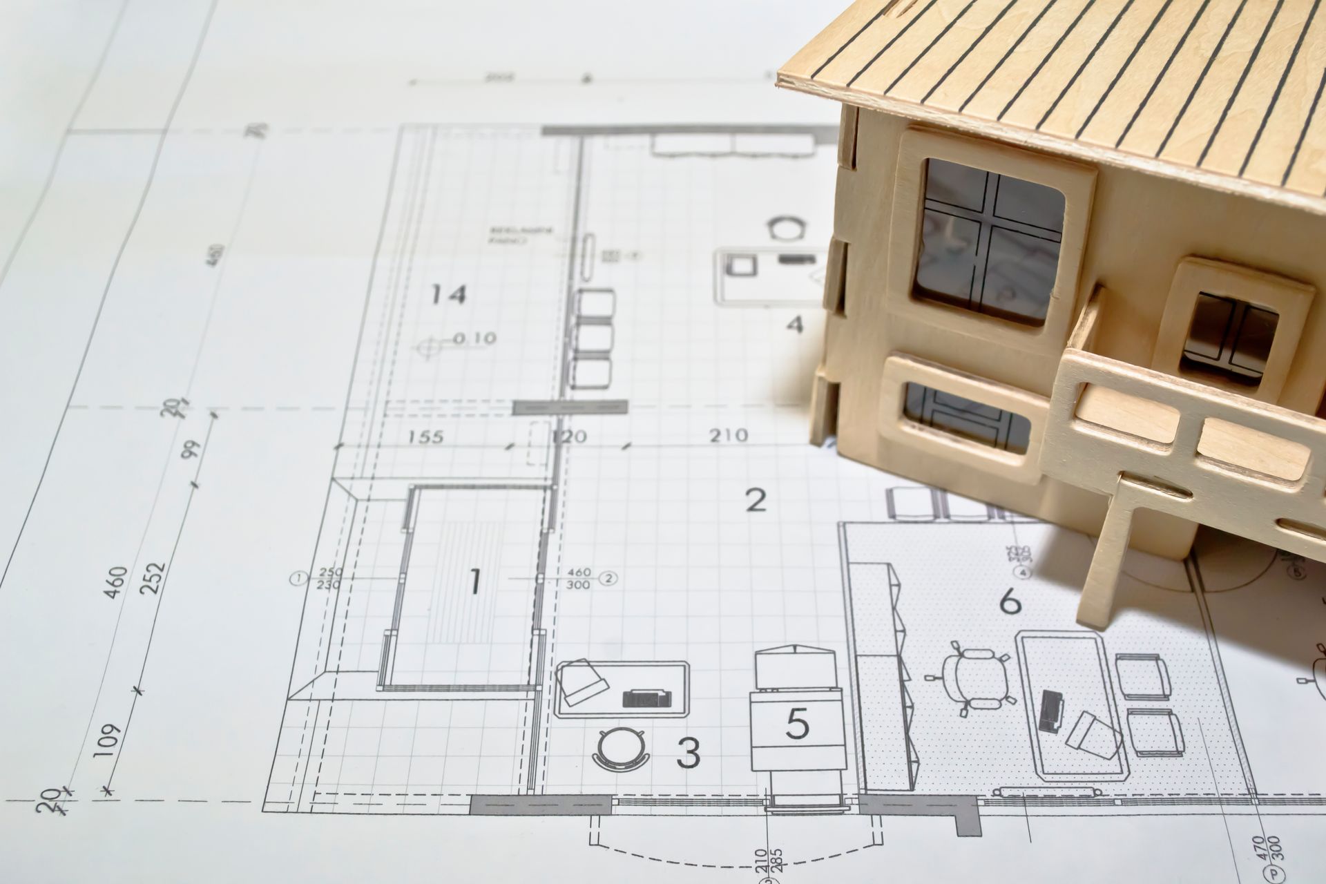 Une maquette de maison en bois repose sur un plan architectural détaillé.