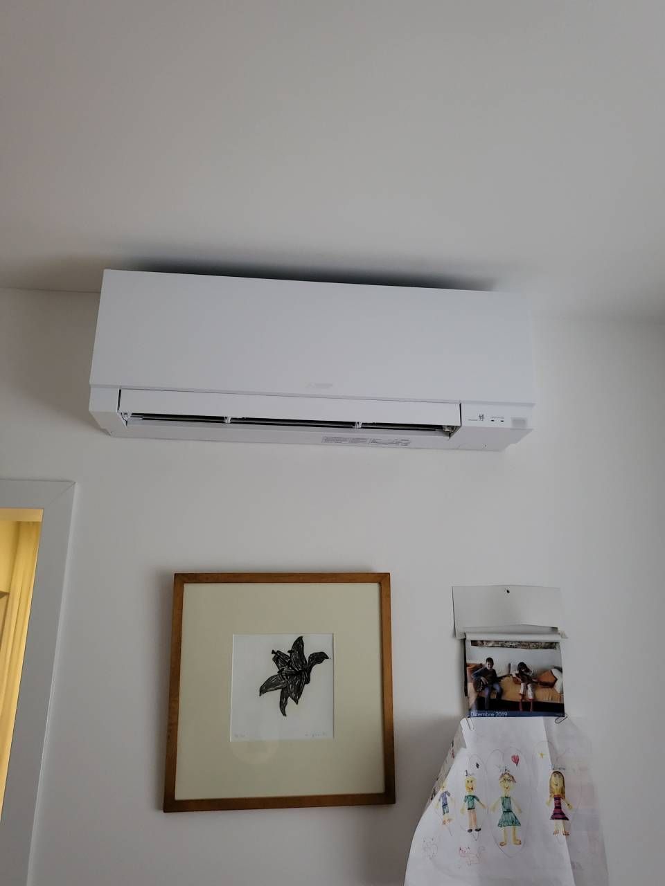In una stanza, un condizionatore d'aria bianco a parete si trova sopra un quadro incorniciato e un piccolo organizer sospeso.