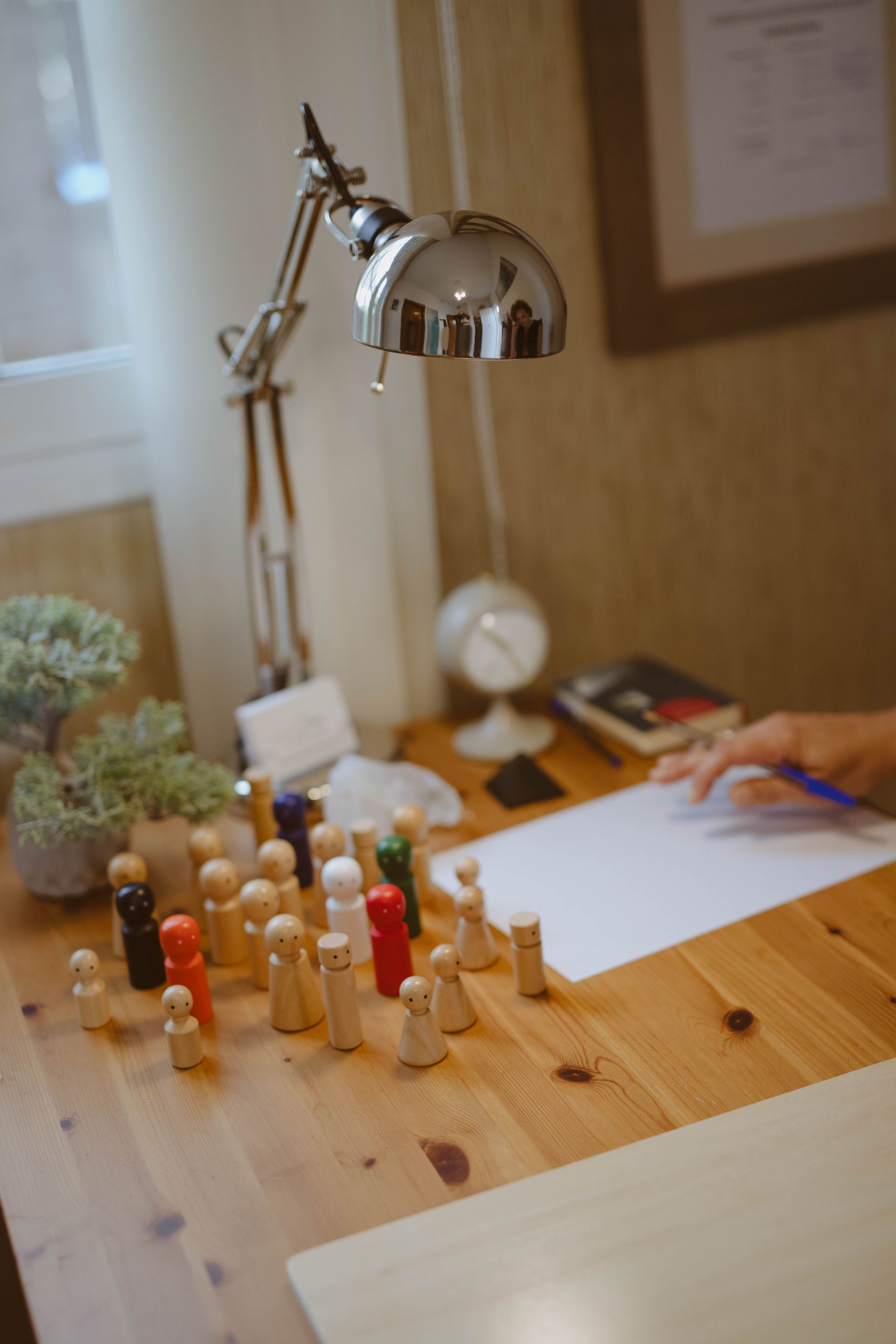 Figuras de madera dispuestas sobre un escritorio junto a una lámpara y papel, escritura a mano.