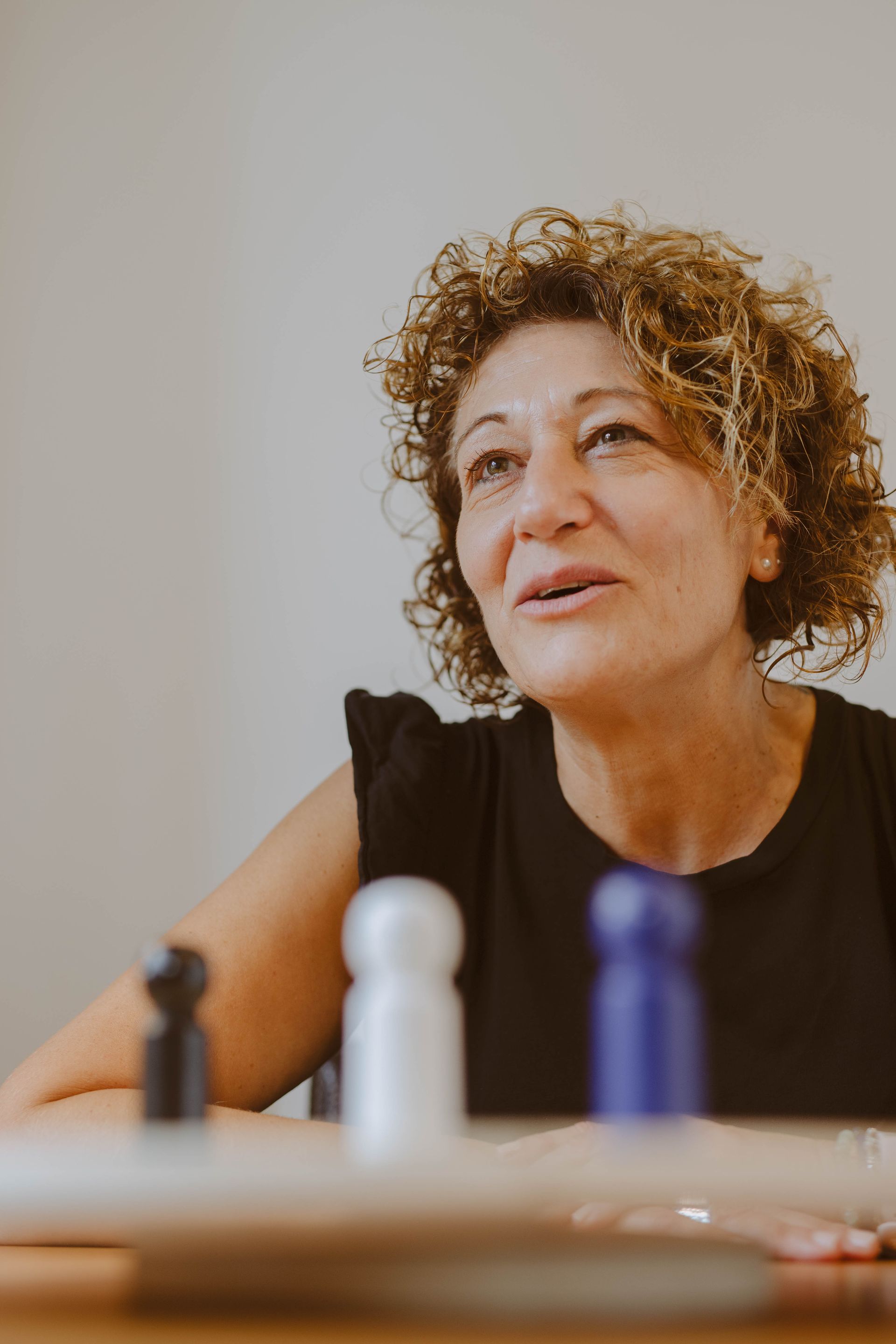 Una mujer con cabello rizado está sentada en una mesa, mirando hacia arriba, jugando un juego de mesa con clavijas de colores