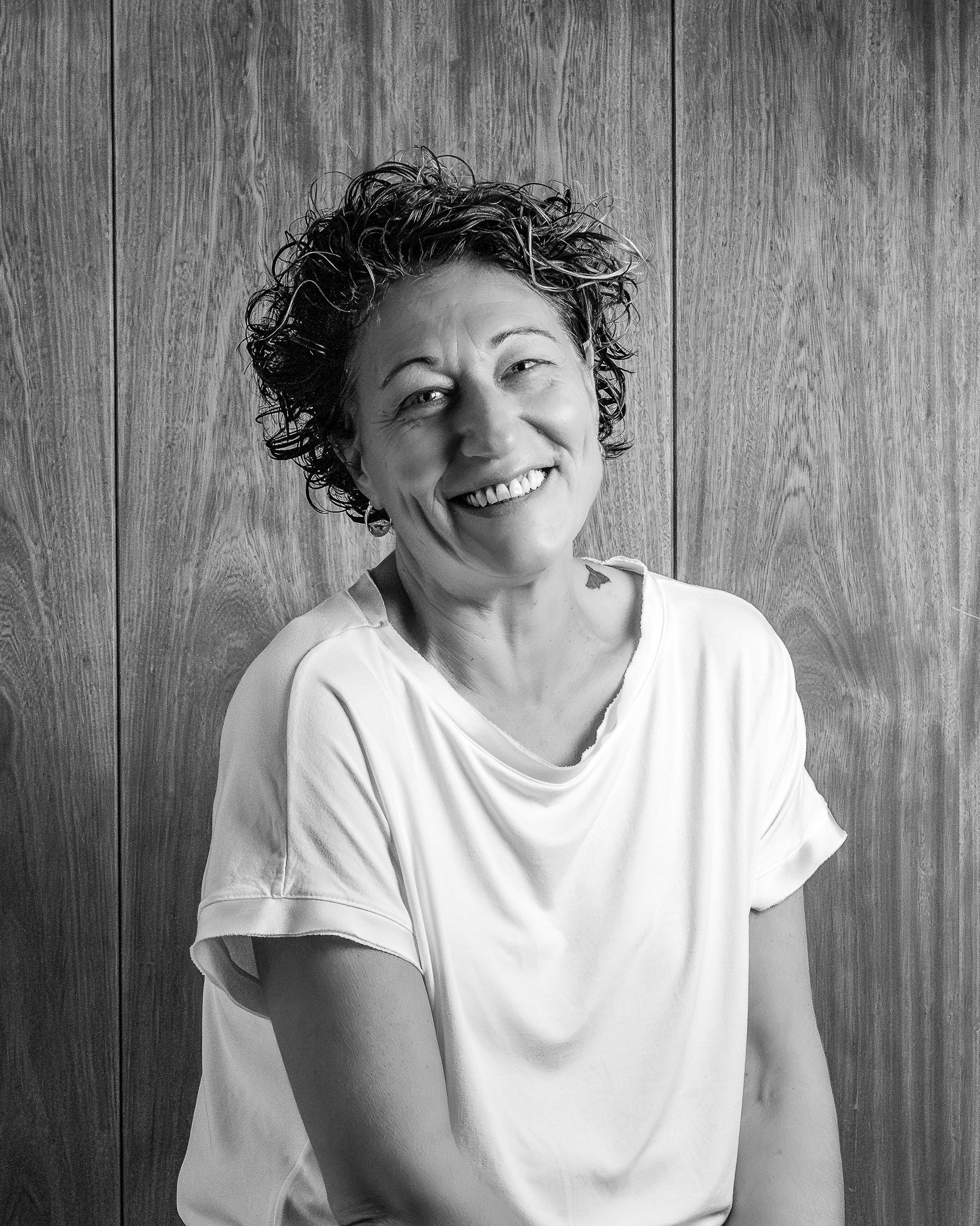 Una mujer con cabello rizado está sentada en una mesa, mirando hacia arriba, jugando un juego de mesa con clavijas de colores