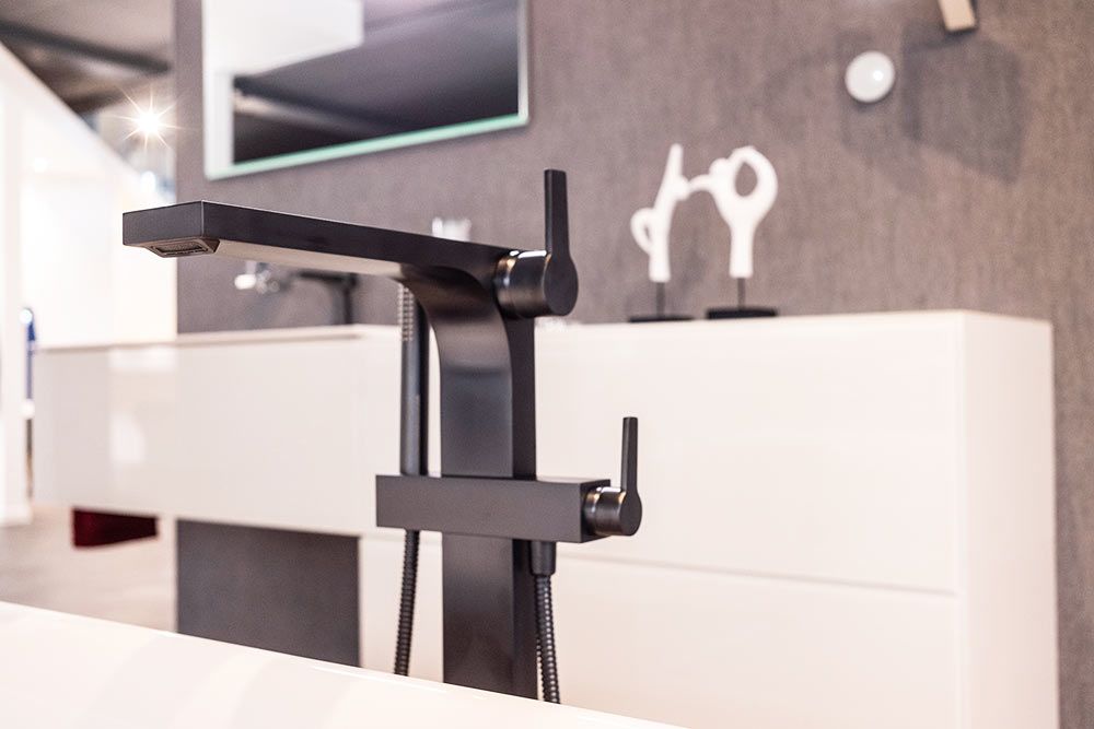 Ein schwarzer Wasserhahn steht auf einer weißen Ablage in einem Badezimmer.
