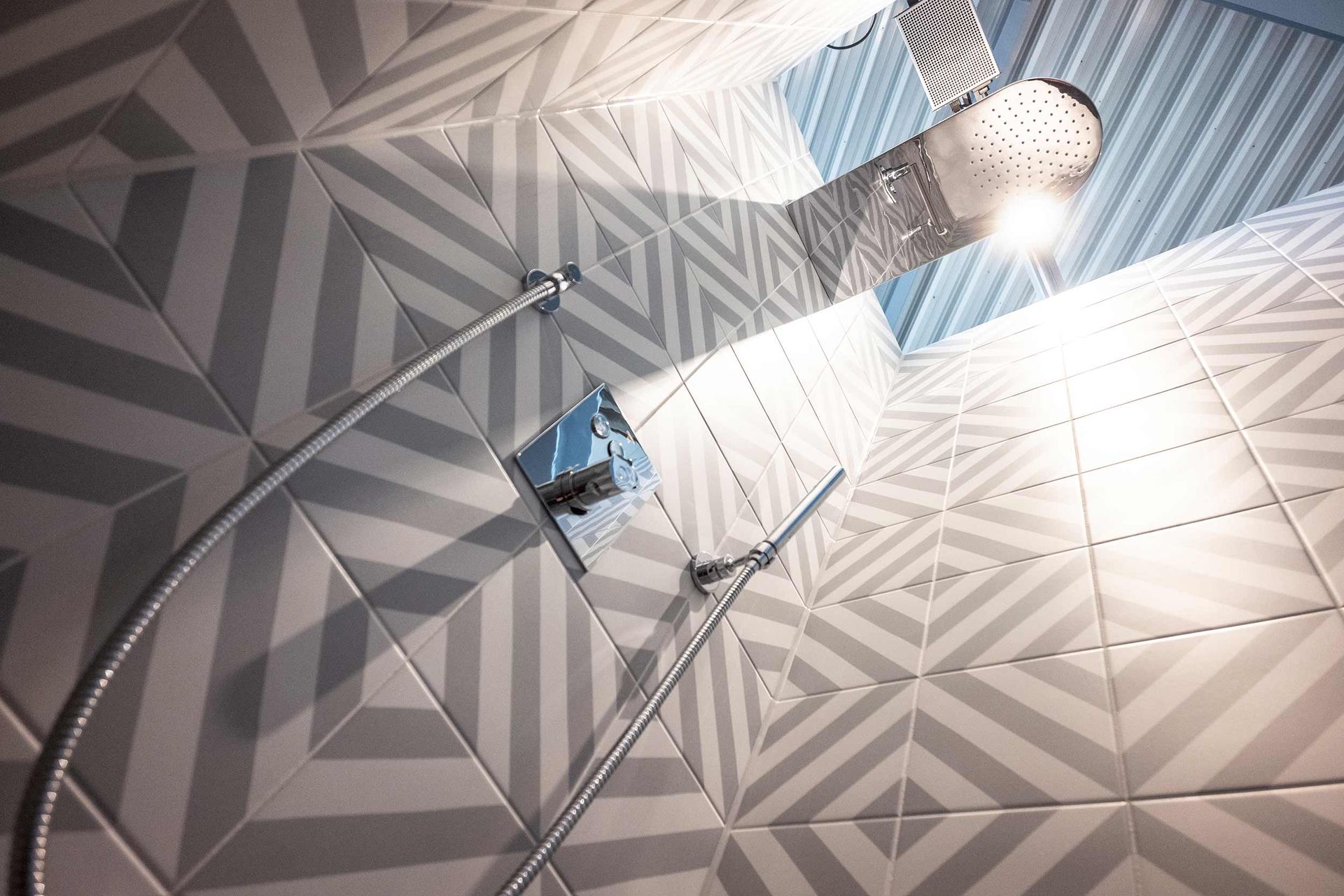 In einem Badezimmer mit geometrischen Fliesen hängt ein Duschkopf von der Decke.