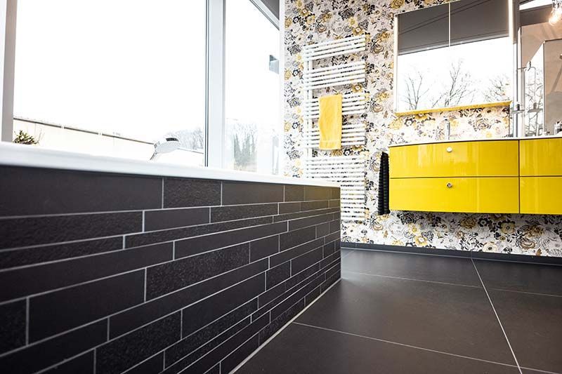 Ein Badezimmer mit schwarzen Fliesen und gelben Schränken