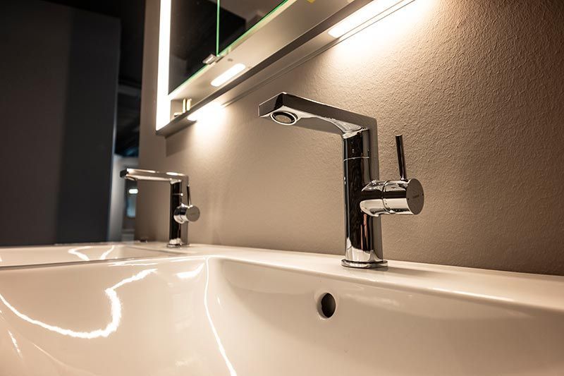 Ein Waschbecken mit zwei Wasserhähnen und einem Spiegel.