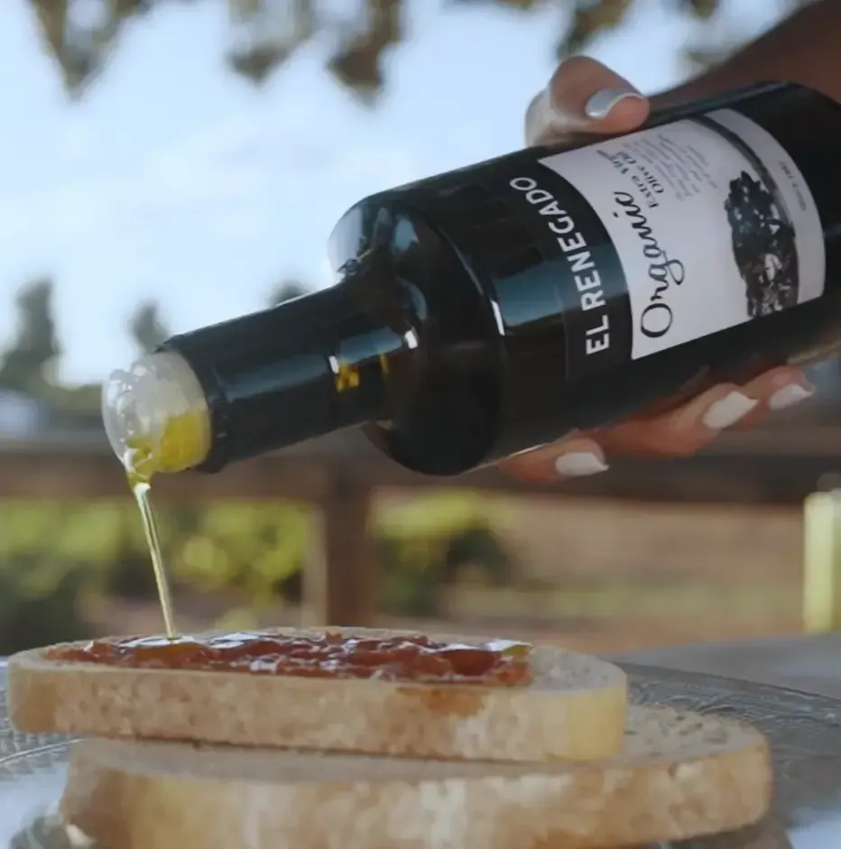 Aceite de oliva vertido sobre pan. Una mano sostiene una botella con la etiqueta 