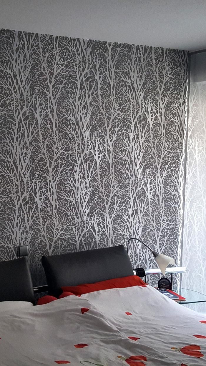 Ein Schlafzimmer mit Bett, Nachttisch, Lampe und Tapete.