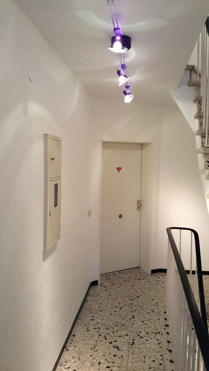 Ein Flur mit einer weißen Tür und violetten Lichtern, die von der Decke hängen.