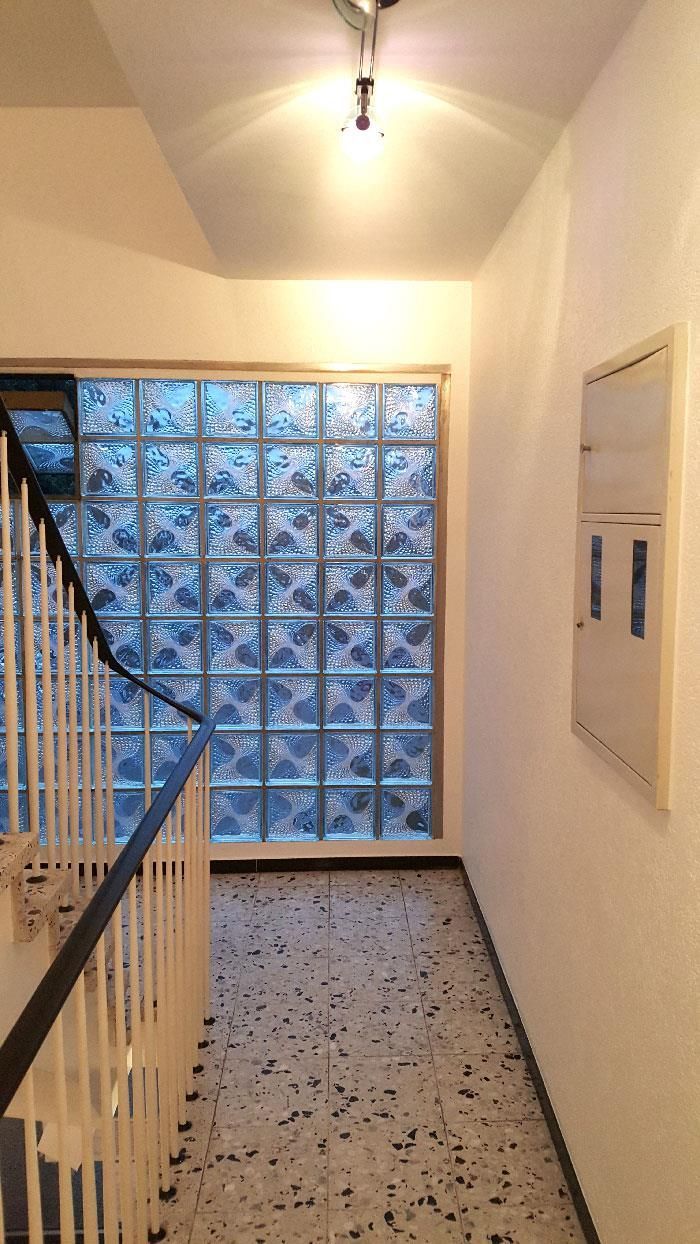 Ein Flur mit einer Treppe und einem Fenster mit Glasbausteinen in der Wand.