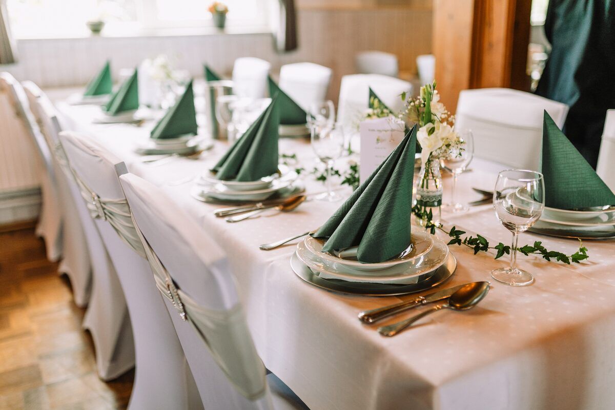 Ein langer Tisch ist für einen Hochzeitsempfang mit grünen Servietten und Tellern gedeckt.